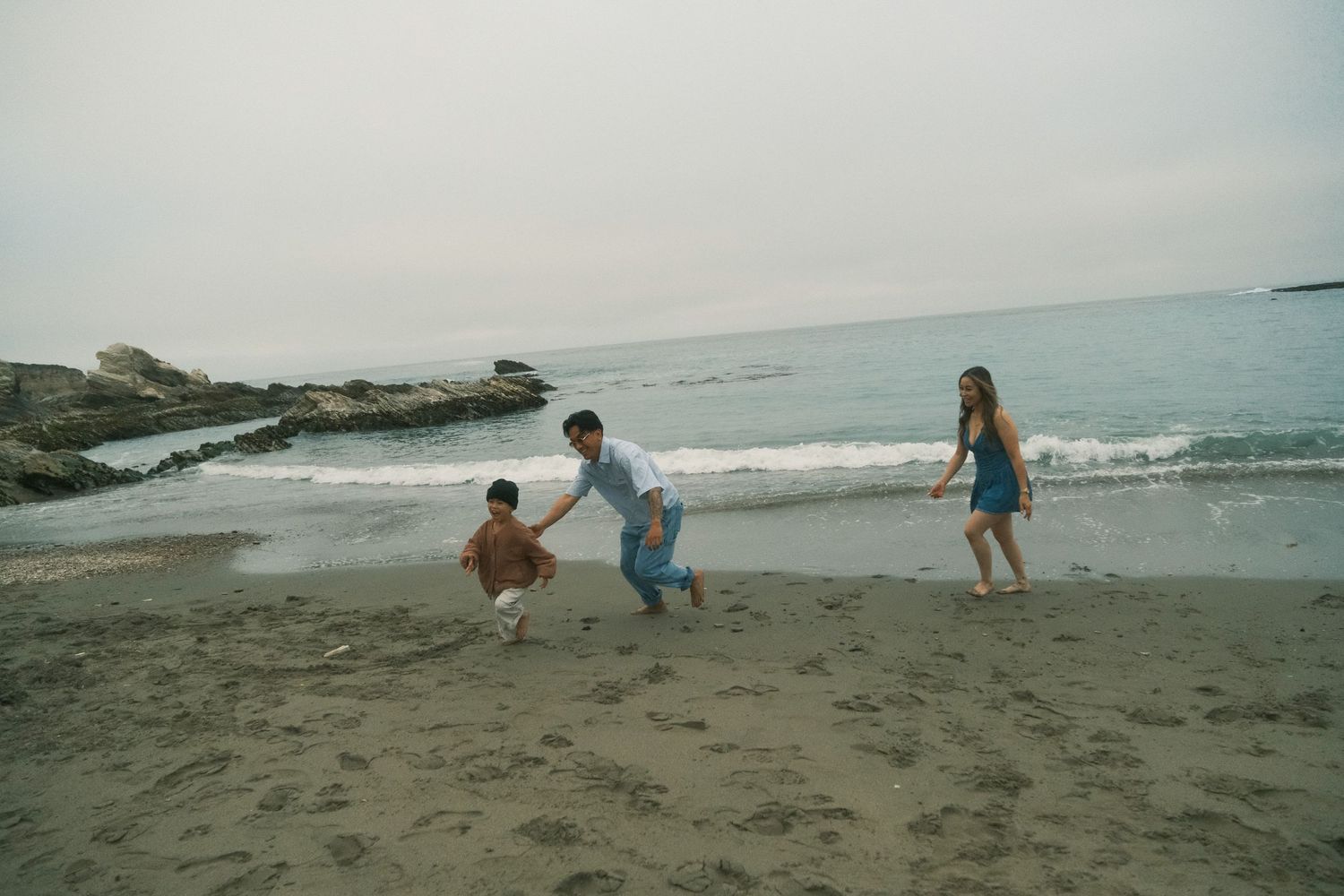 Children playing chase games on a wide sandy beach with waves rolling in.