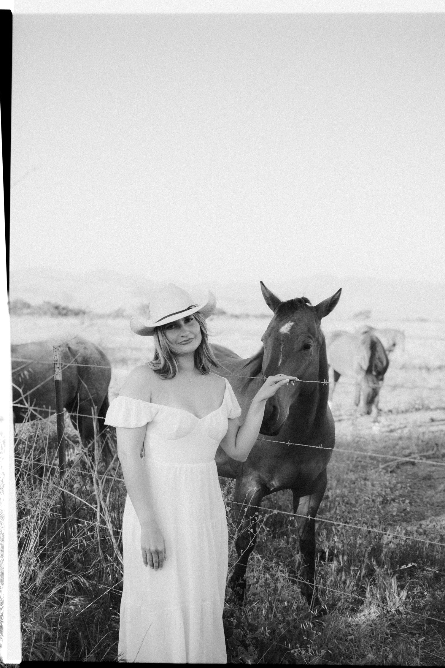 Black and white artistic shots of someone in white standing beside a horse in nature.
