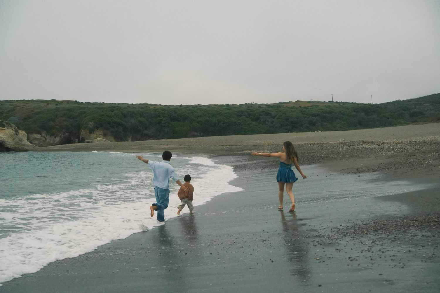People enjoying a scenic day at the beach with rocky cliffs and rolling waves in the background.