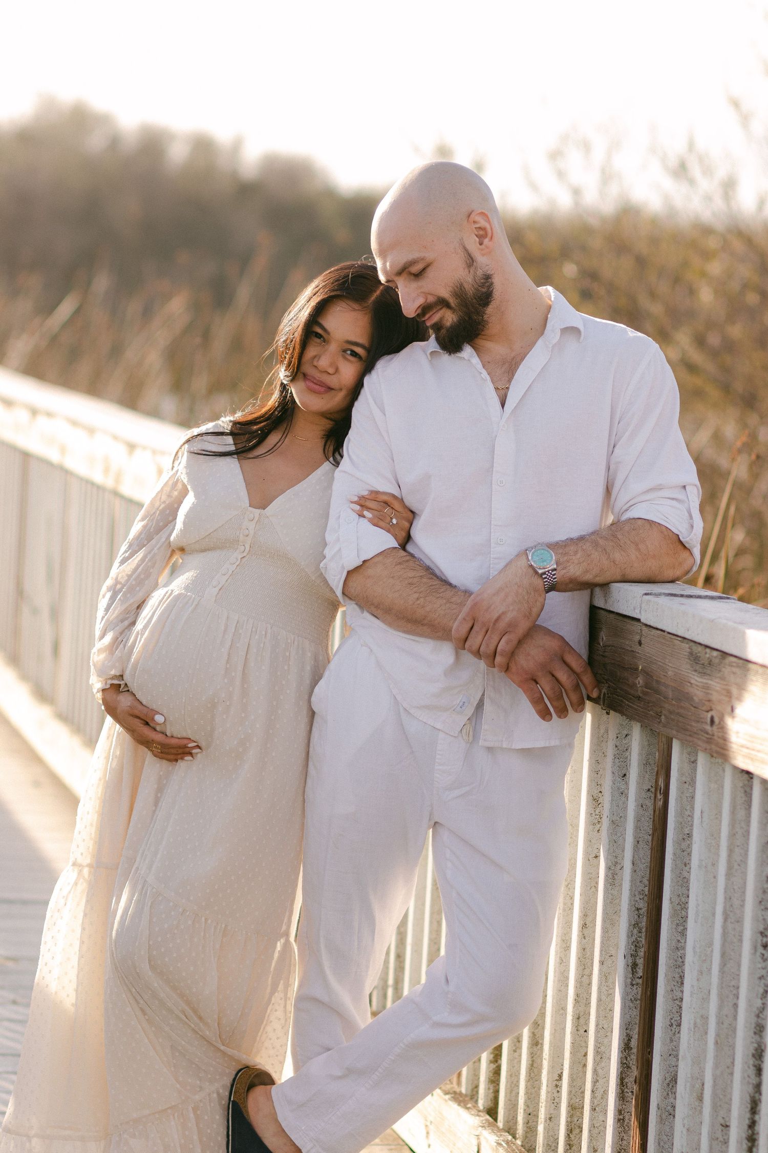 Expecting couple shares tender moments during golden hour photoshoot on a boardwalk.
