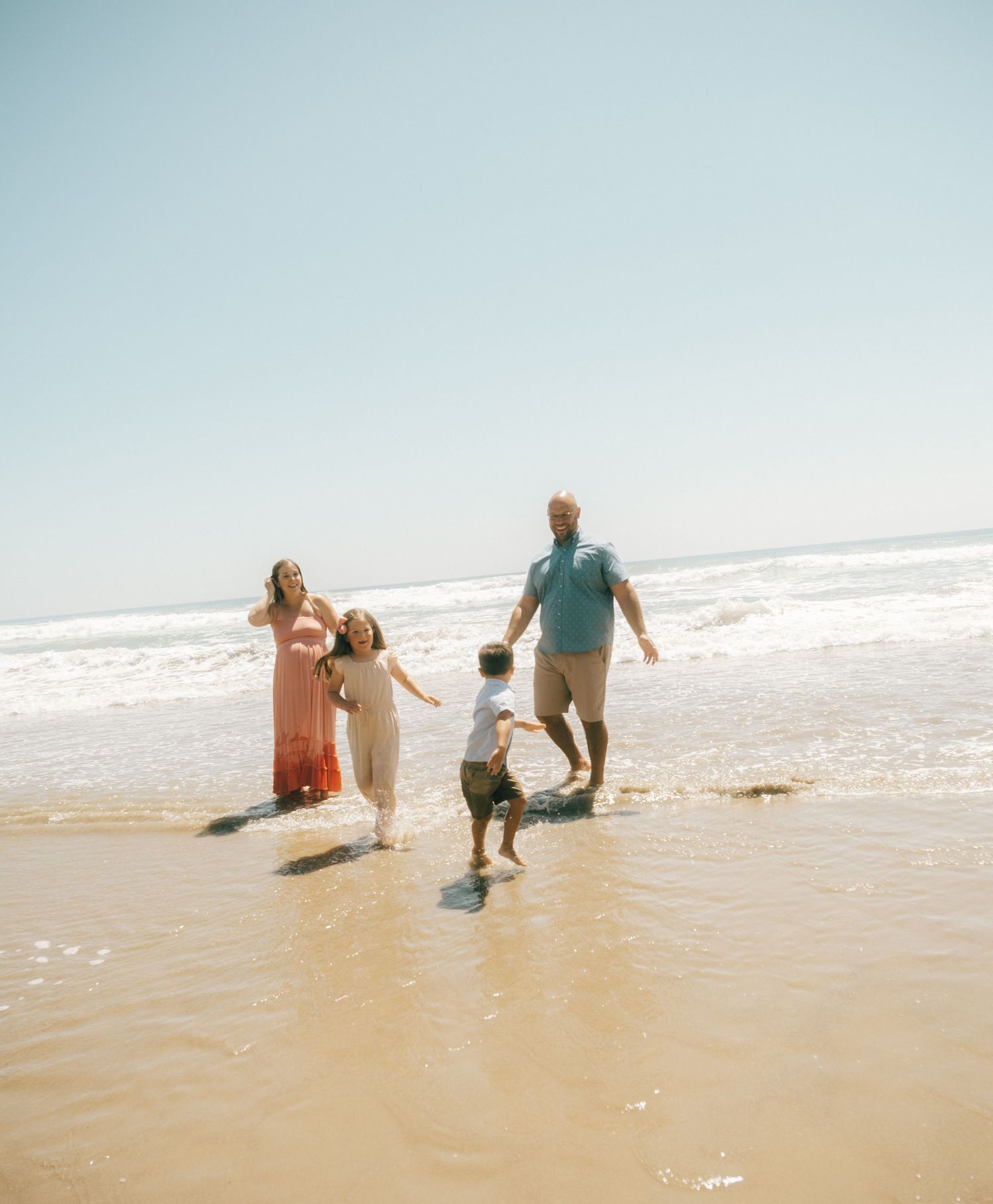 Family of four playing in ocean waves on a sunny beach, parents and two young children enjoying a seaside vacation.