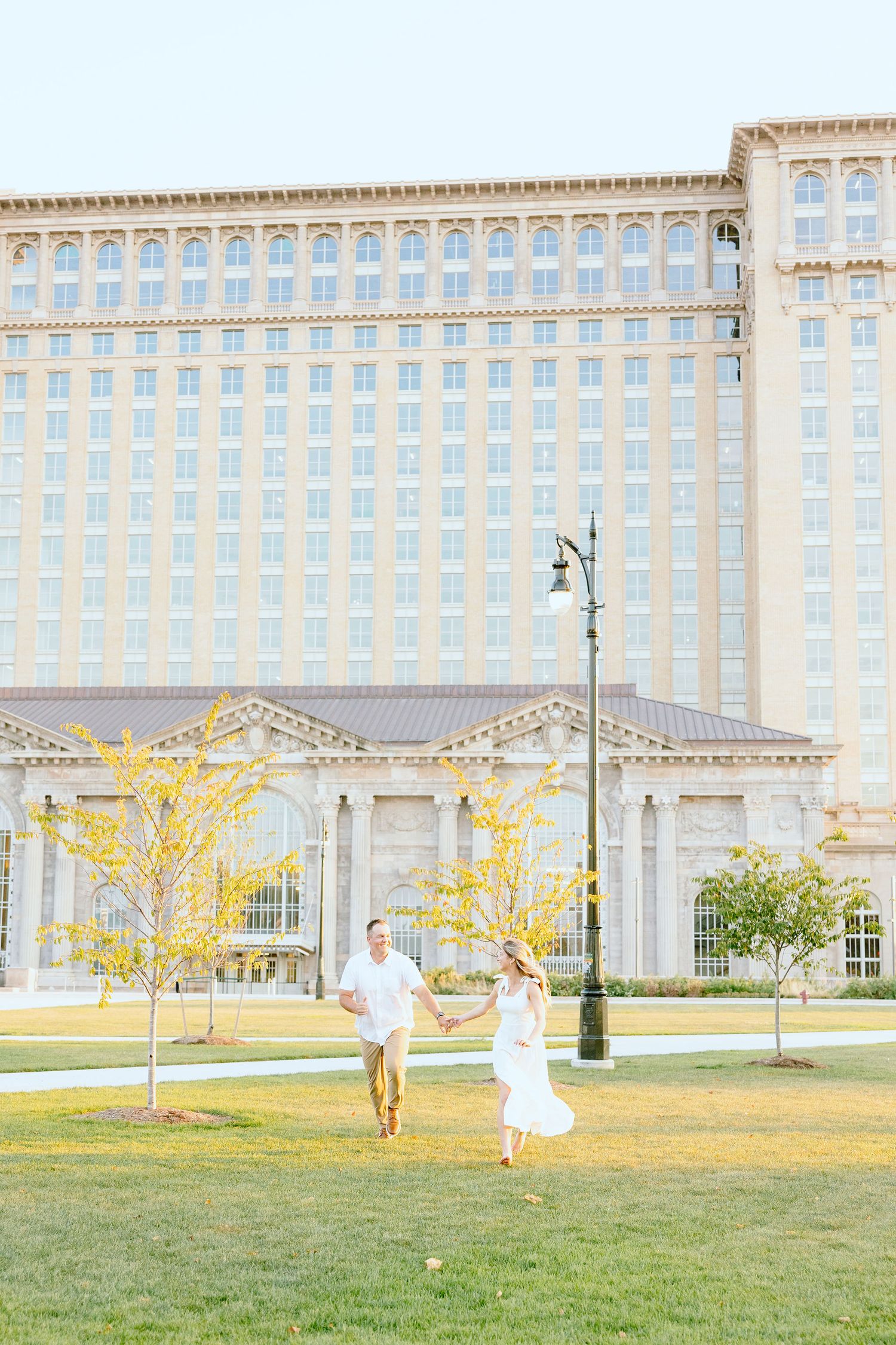 Engaged couple running and holding hands at Michigan Central Station summer engagement session in Detroit, MI