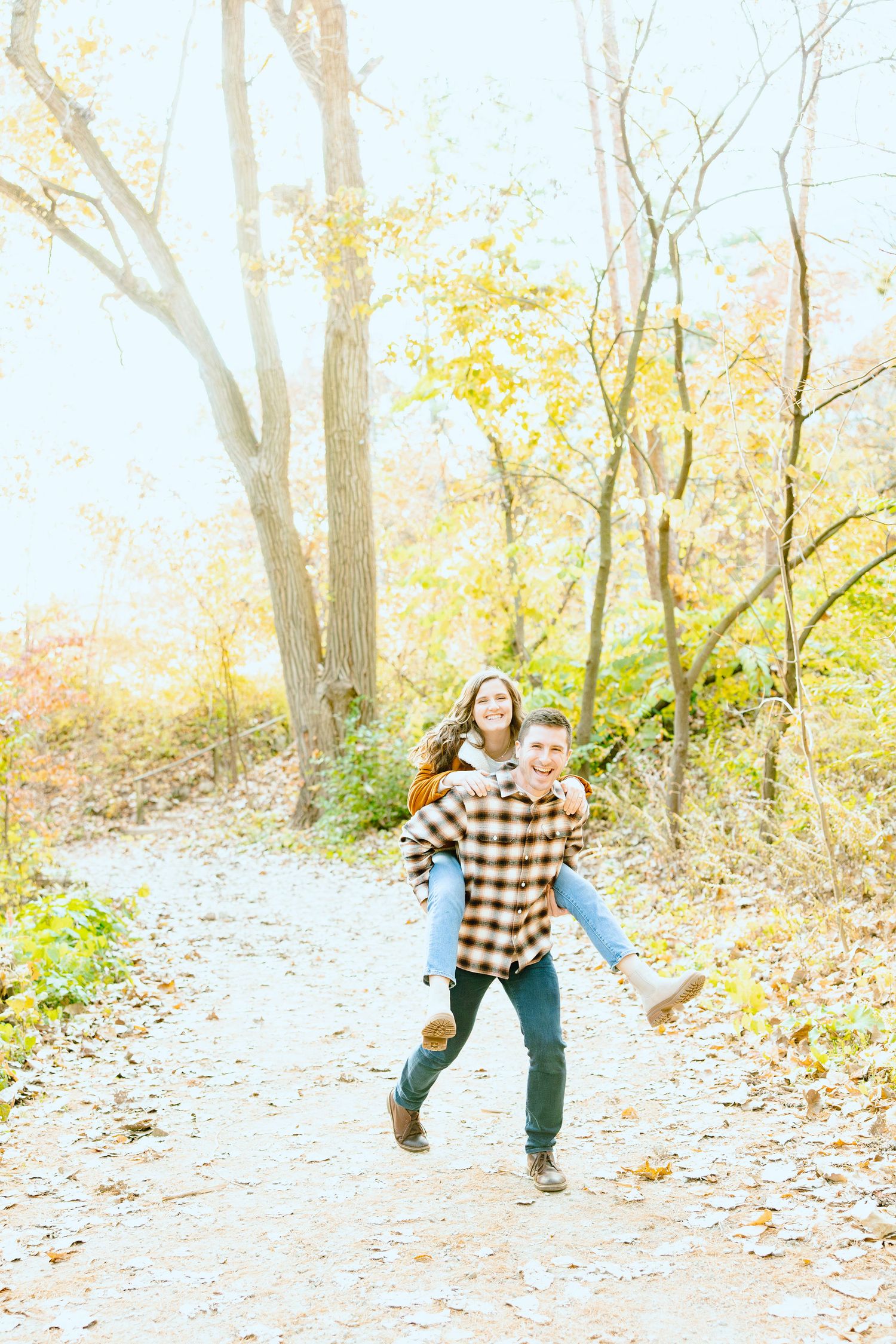 Man giving woman piggyback ride in forest at Nichols Arboretum fall engagement session in Ann Arbor, MI