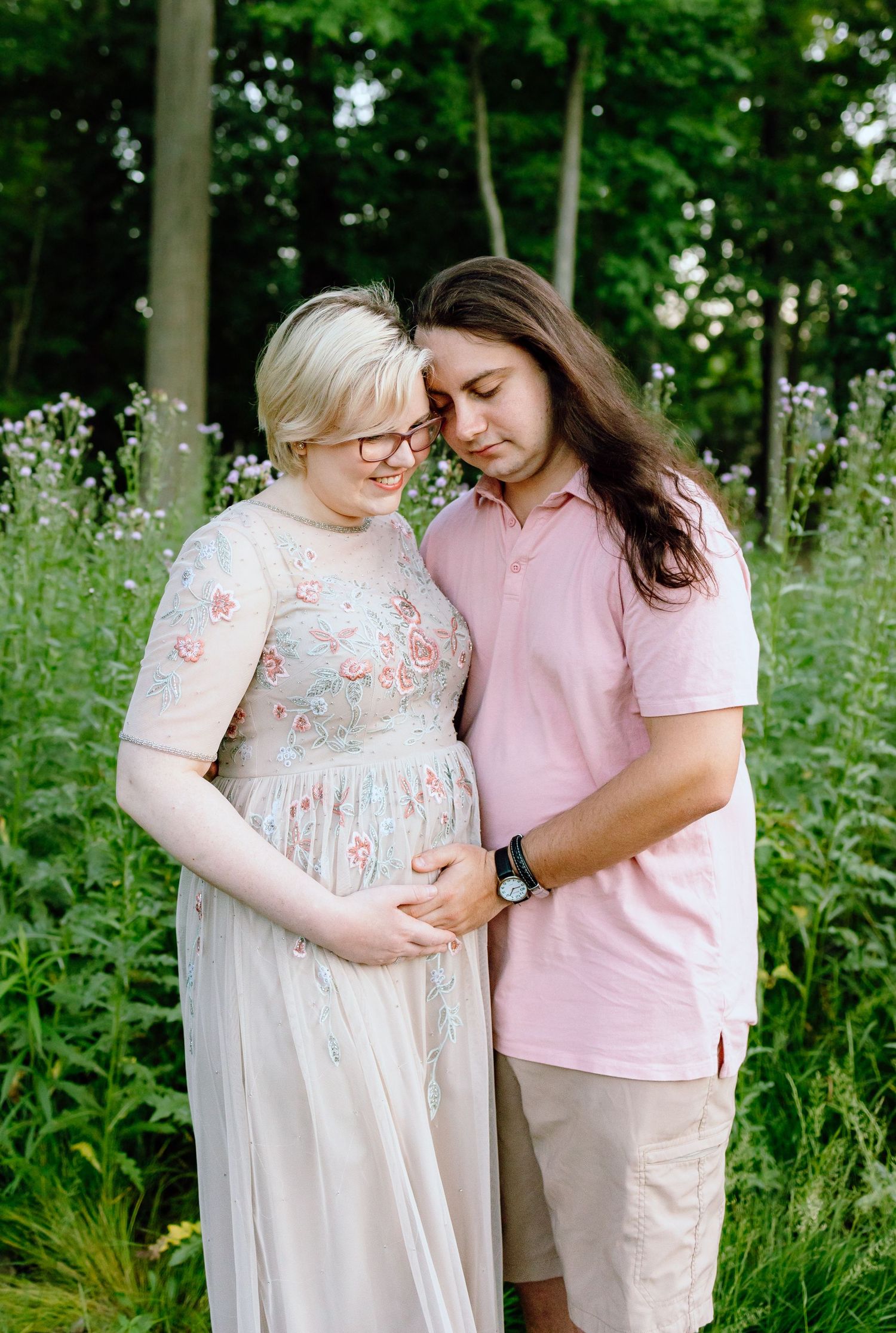 Pregnant couple embracing in front of thistle bush in Beverly Hills Village Park, MI