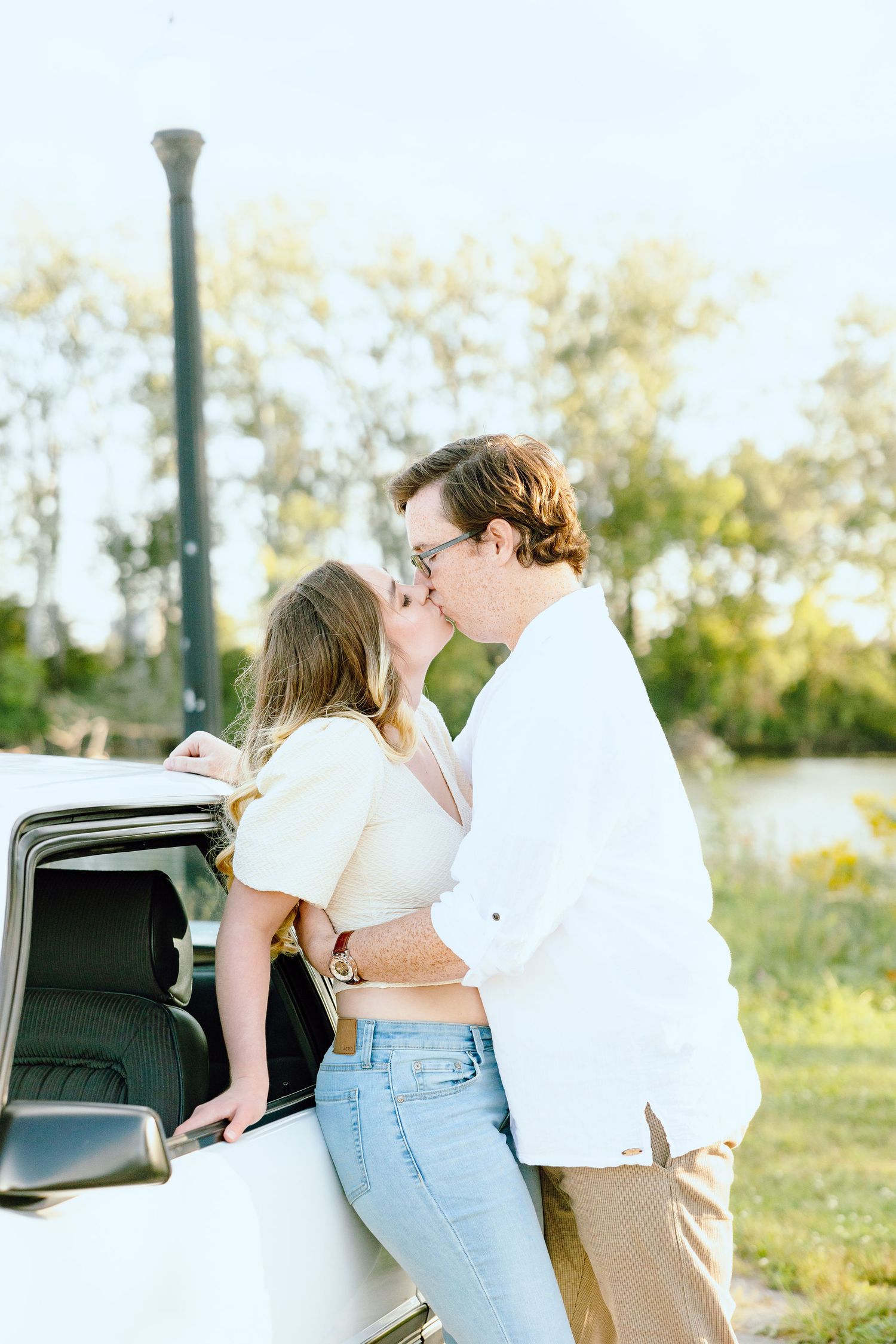 Engaged couple kissing against vintage car at Belle Isle summer engagement session in Detroit, MI