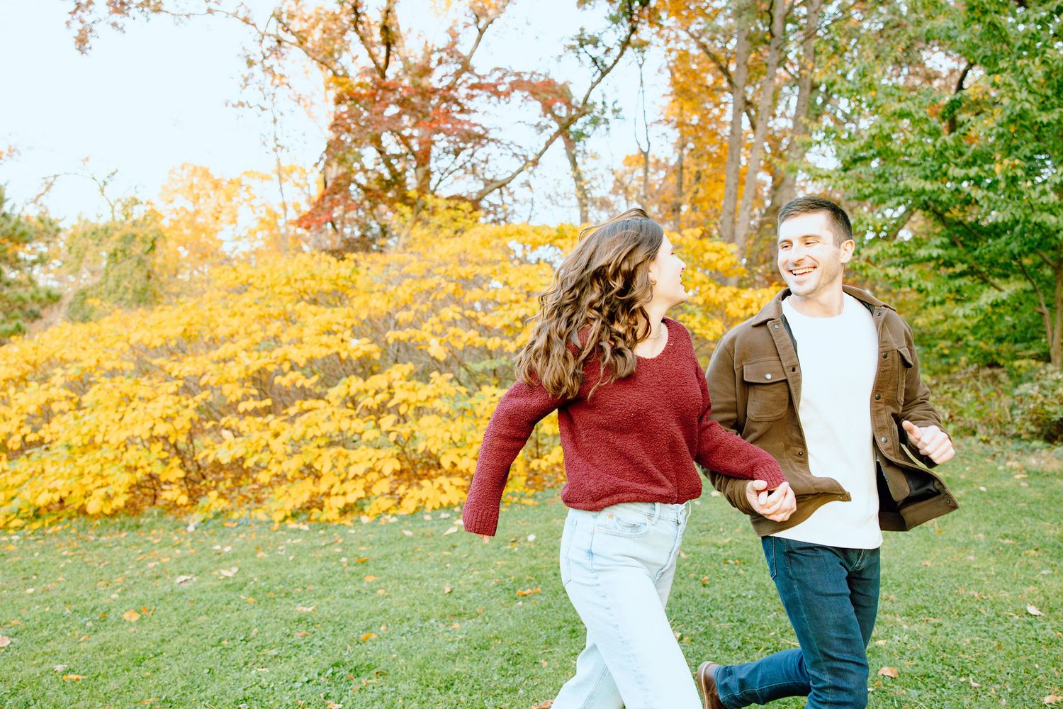 Engaged couple running and holding hands at Nichols Arboretum fall engagement session in Ann Arbor, MI