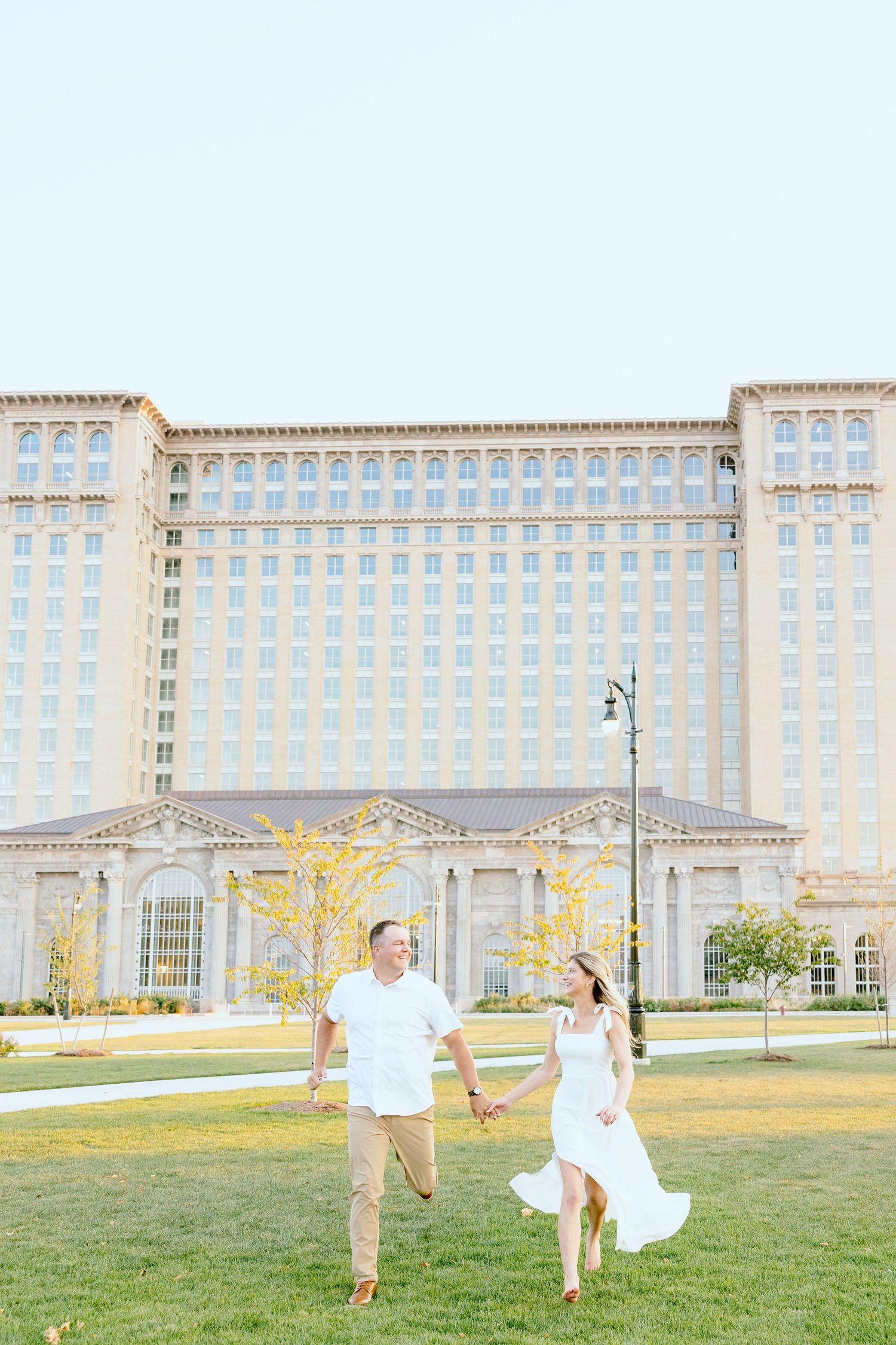 Engaged couple running and holding hands at Michigan Central Station summer engagement session in Detroit, MI