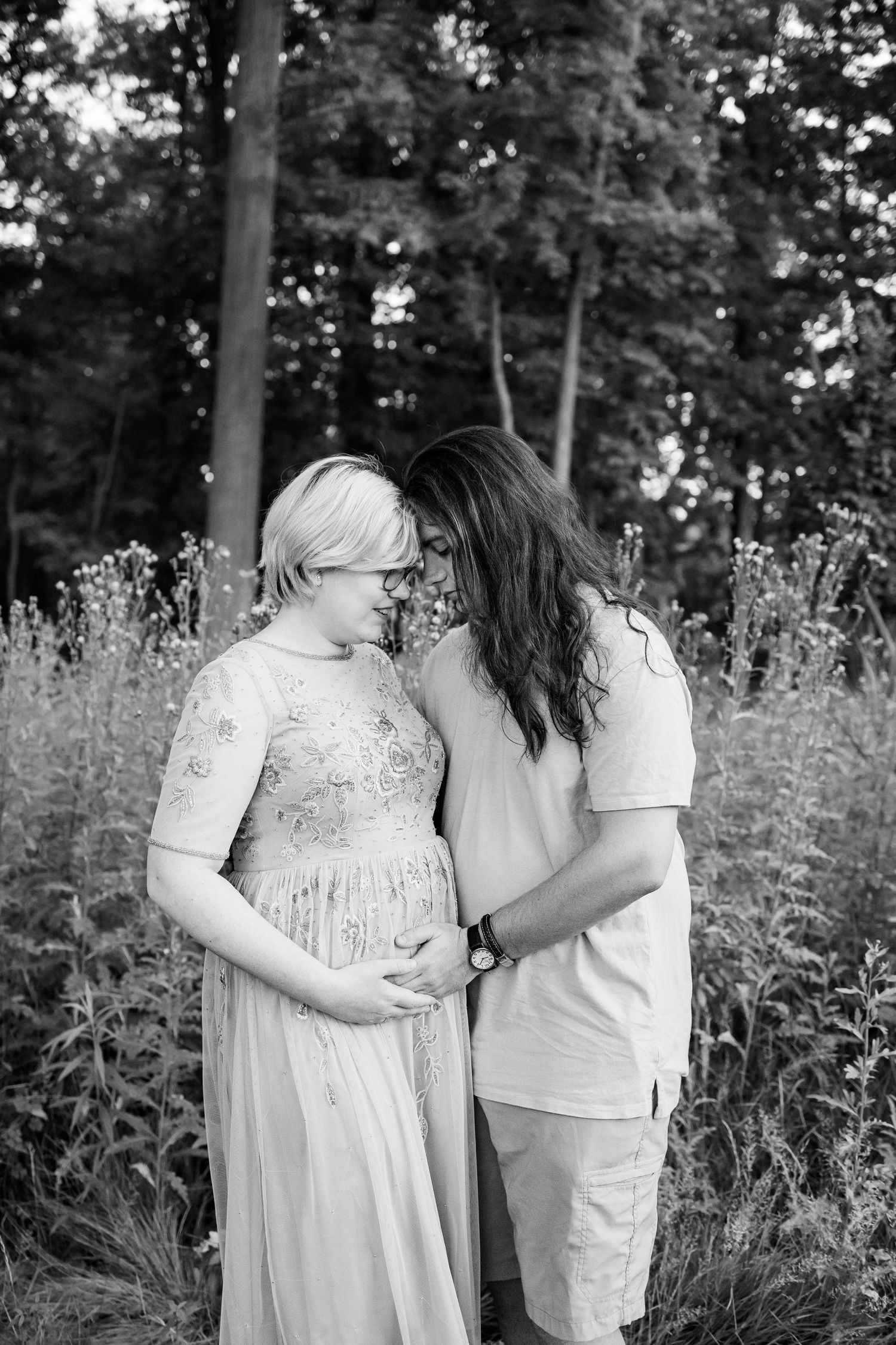 Pregnant couple embracing in front of thistle bush in Beverly Hills Village Park, MI