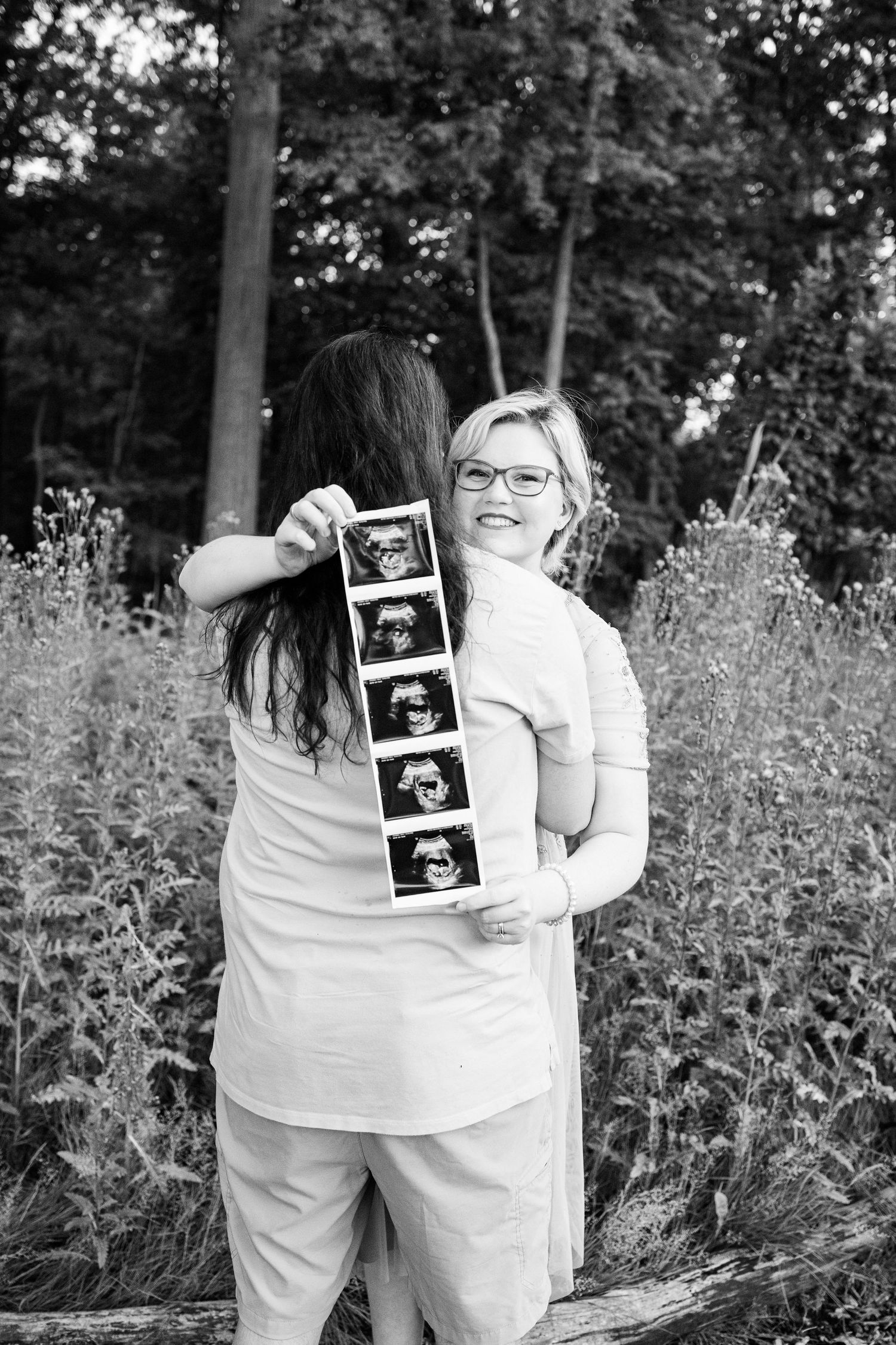 Pregnant couple holding ultrasound photo in front of thistle bush in Beverly Hills Village Park, MI
