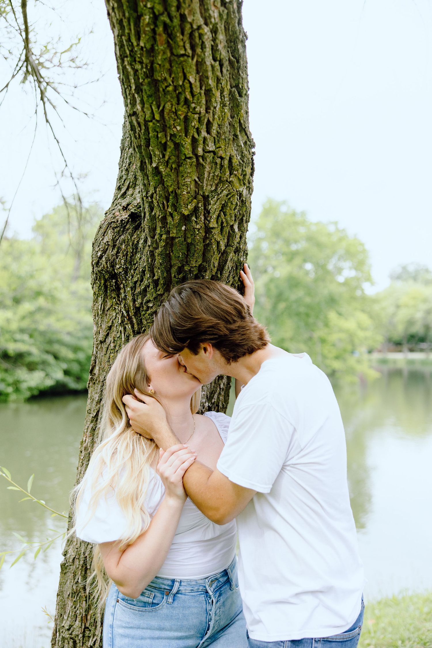Engaged couple kissing against tree at Greenfield Village in Dearborn, MI
