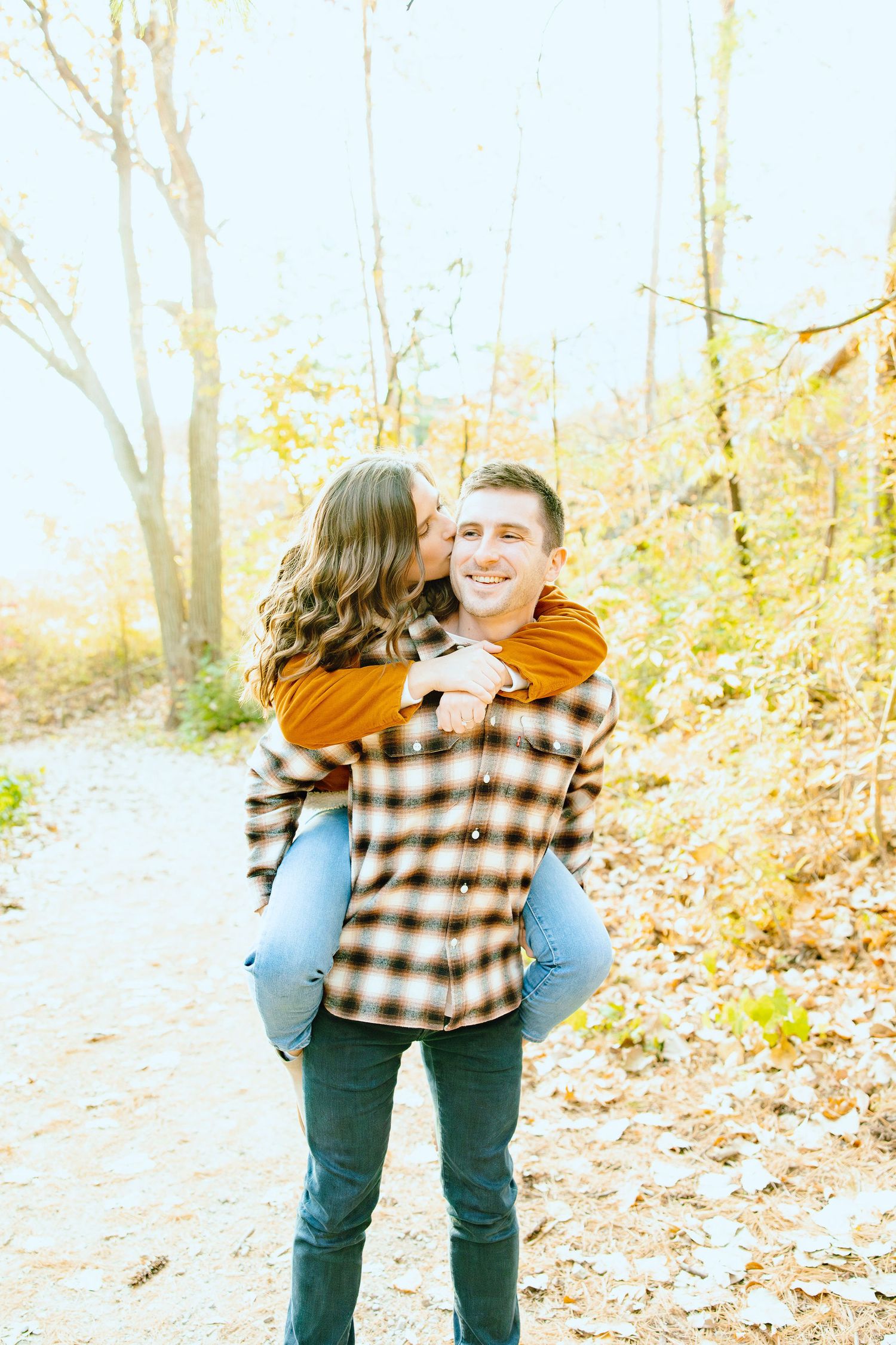 Man giving woman piggyback ride in forest at Nichols Arboretum fall engagement session in Ann Arbor, MI