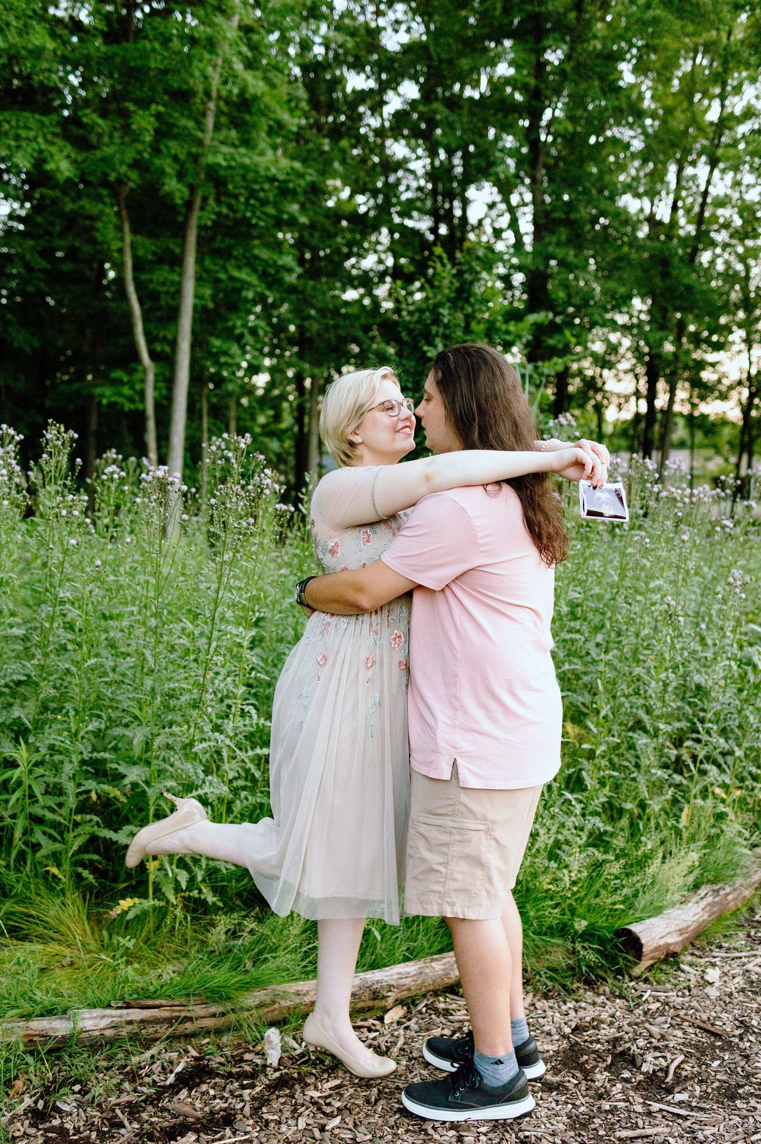 Pregnant couple embracing in front of thistle bush in Beverly Hills Village Park, Michigan
