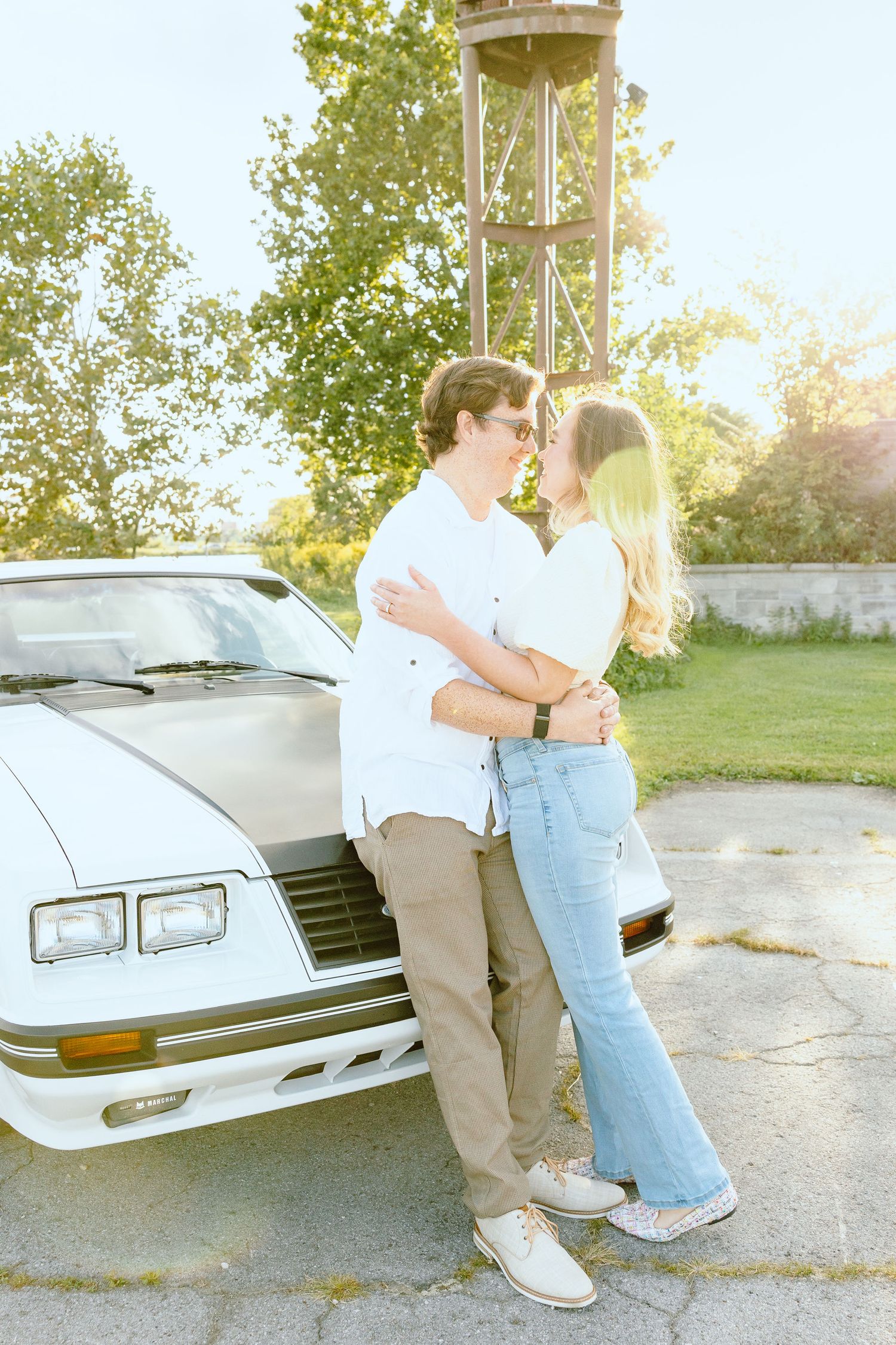 Engaged couple embracing against vintage car at Belle Isle summer engagement session in Detroit, MI