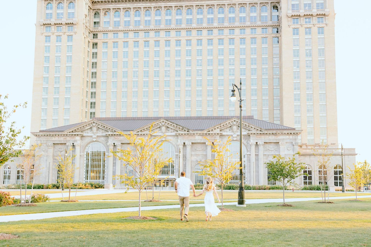 Engaged couple running and holding hands at Michigan Central Station summer engagement session in Detroit, MI