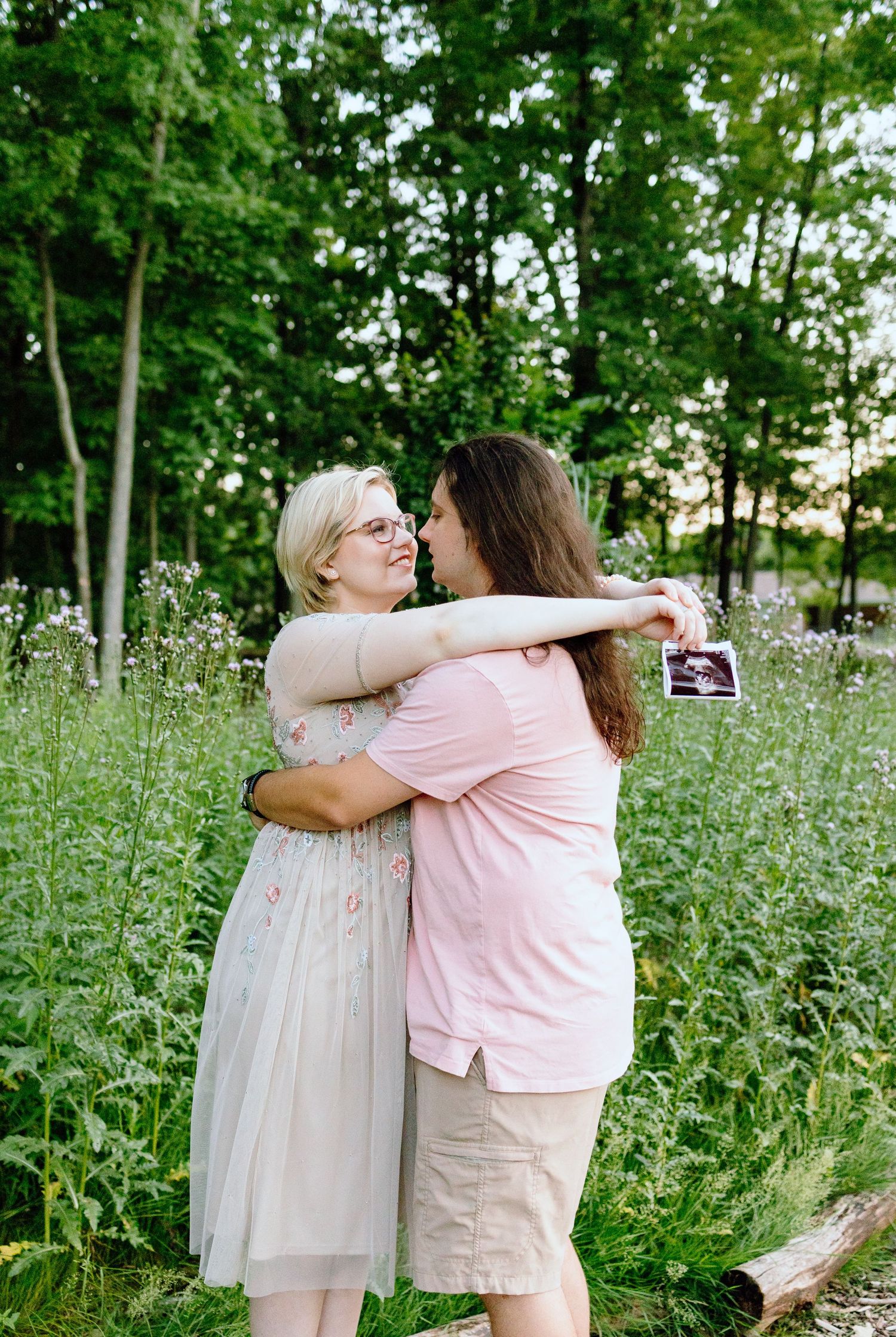Pregnant couple embracing in front of thistle bush in Beverly Hills Village Park, Michigan