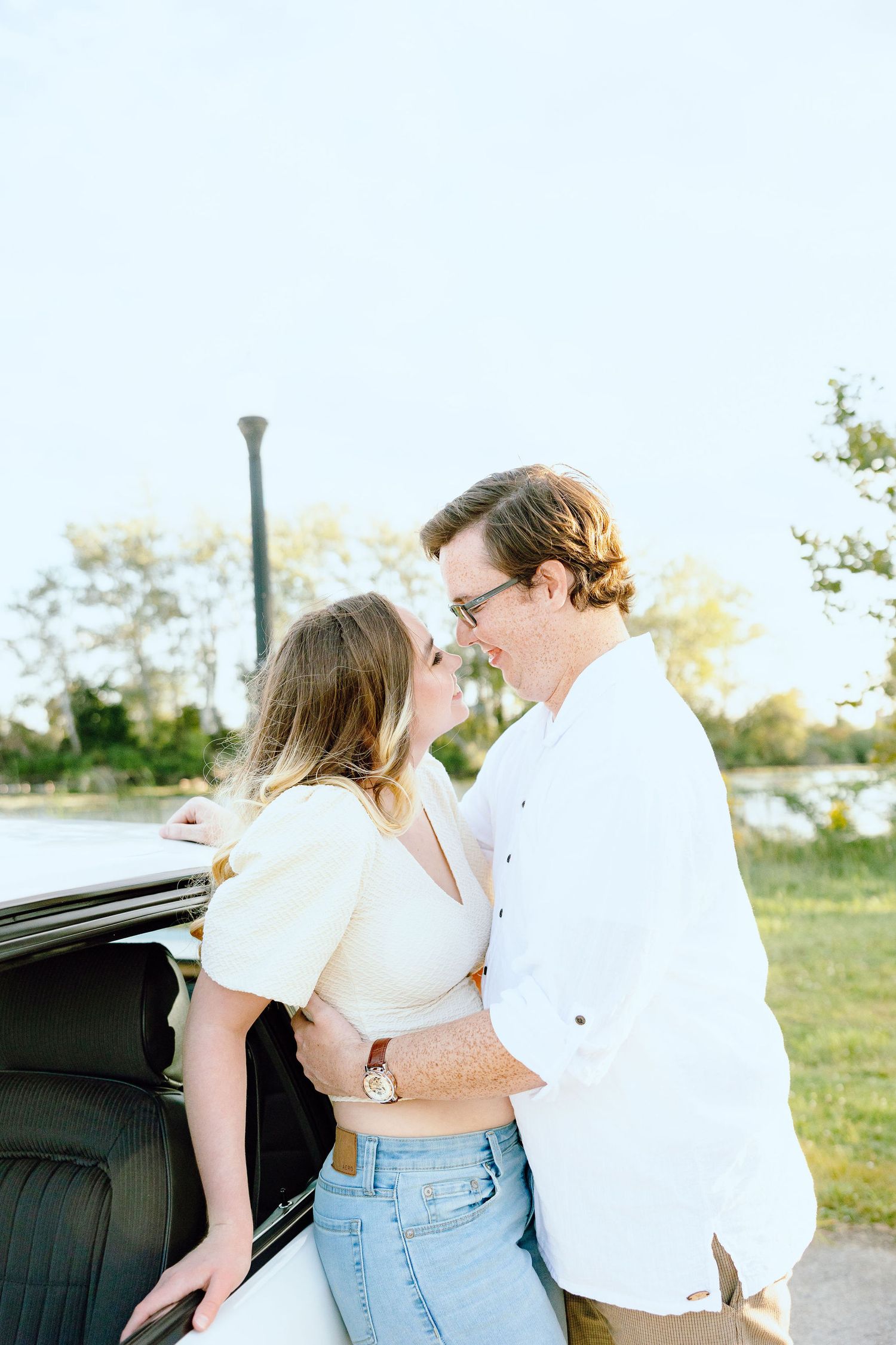 Engaged couple embracing against vintage car at Belle Isle summer engagement session in Detroit, MI