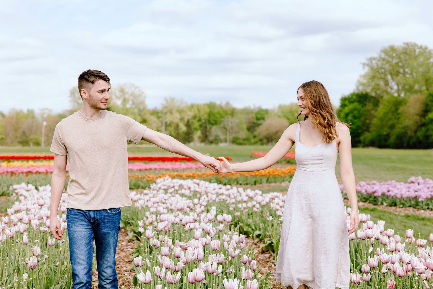 Engaged couple walking and holding hands at DeBuck's tulip field spring engagement session in Belleville, MI