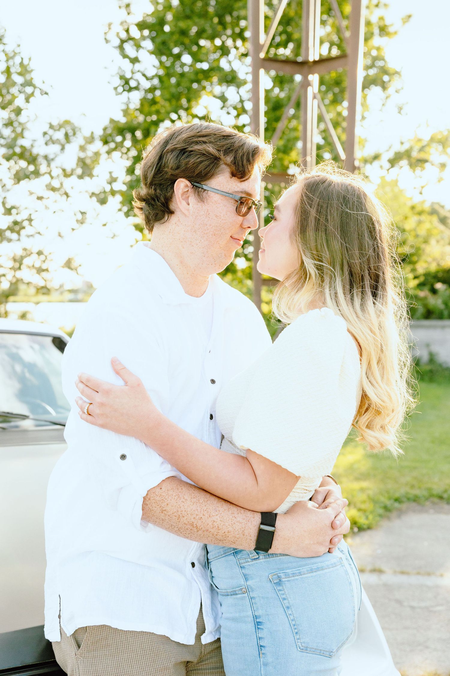 Engaged couple embracing against vintage car at Belle Isle summer engagement session in Detroit, MI