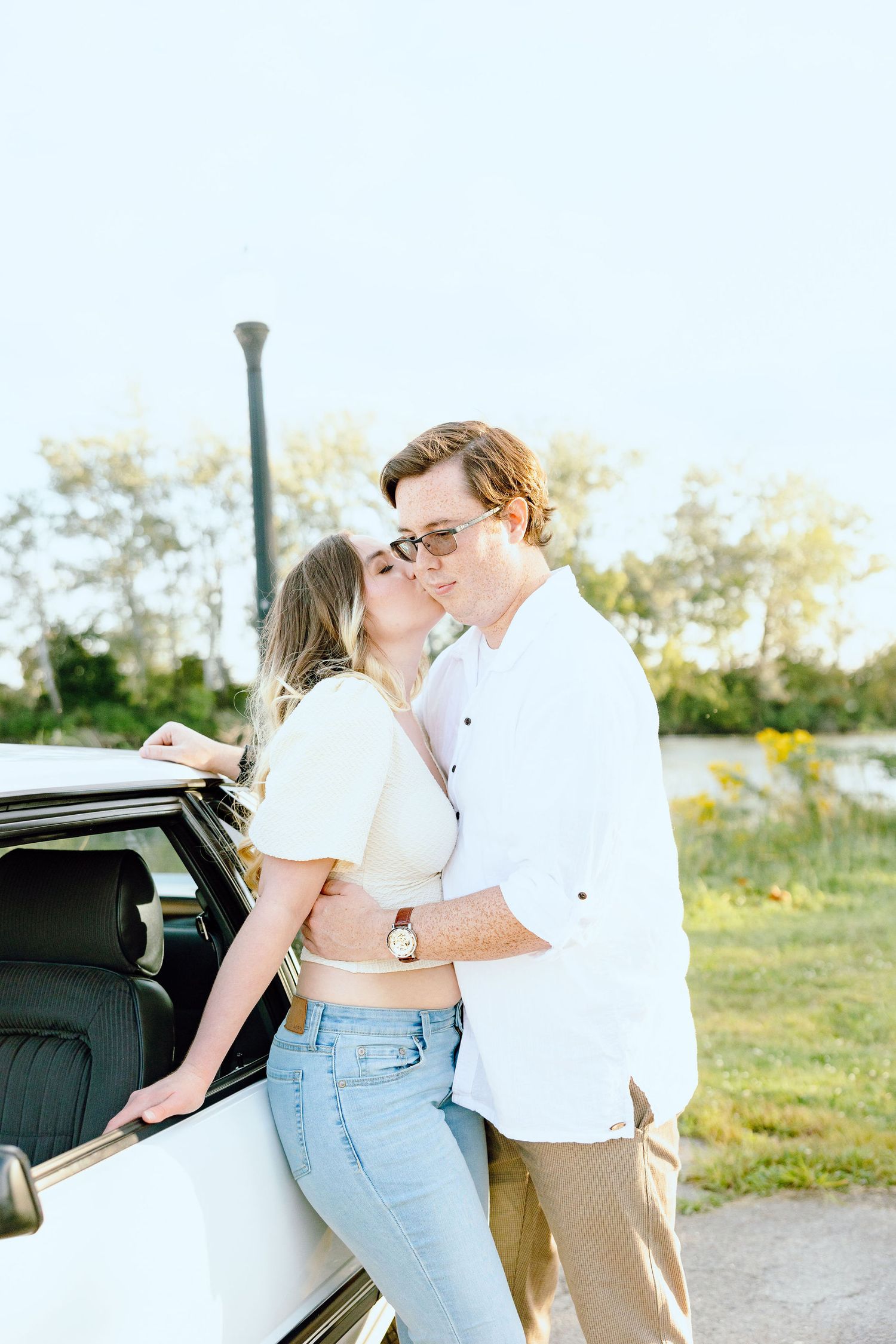 Engaged couple kissing against vintage car at Belle Isle summer engagement session in Detroit, MI