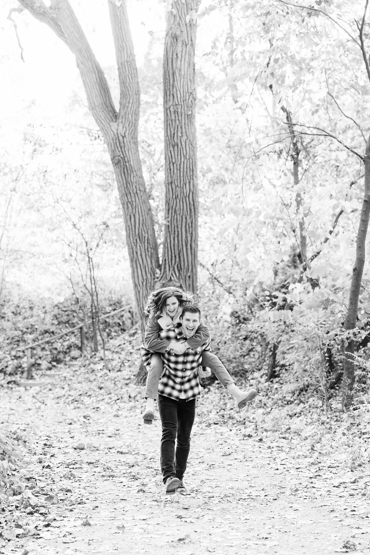 Man giving woman piggyback ride in forest at Nichols Arboretum fall engagement session in Ann Arbor, MI