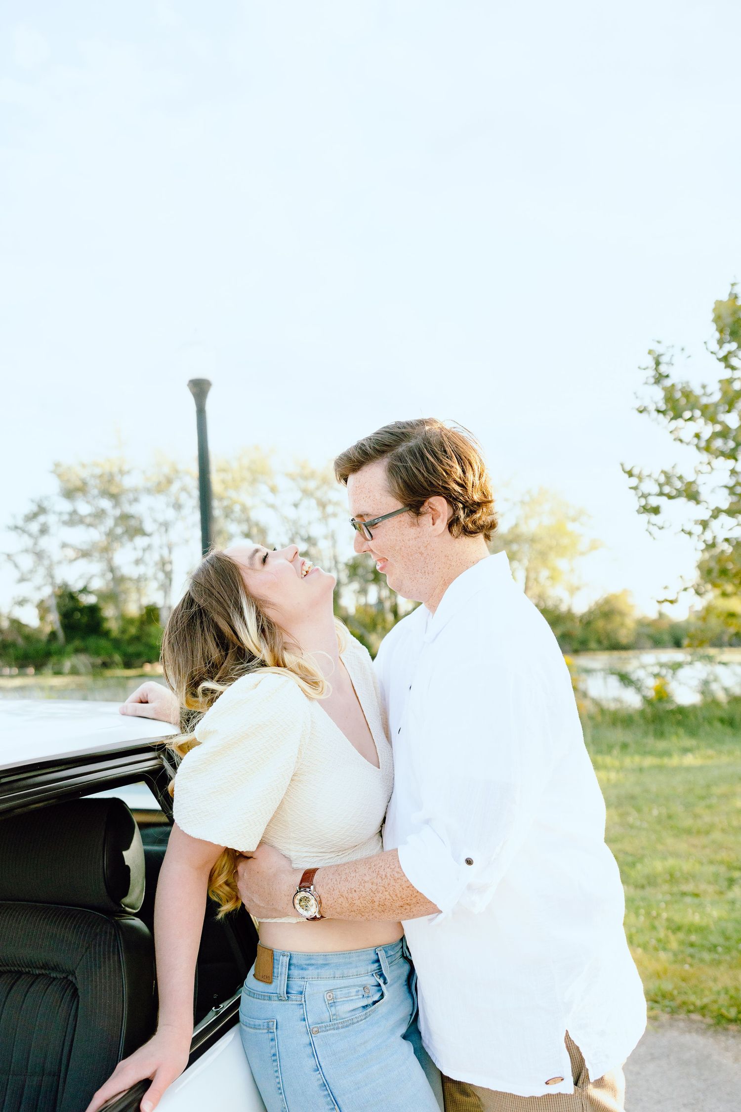 Engaged couple embracing against vintage car at Belle Isle summer engagement session in Detroit, MI