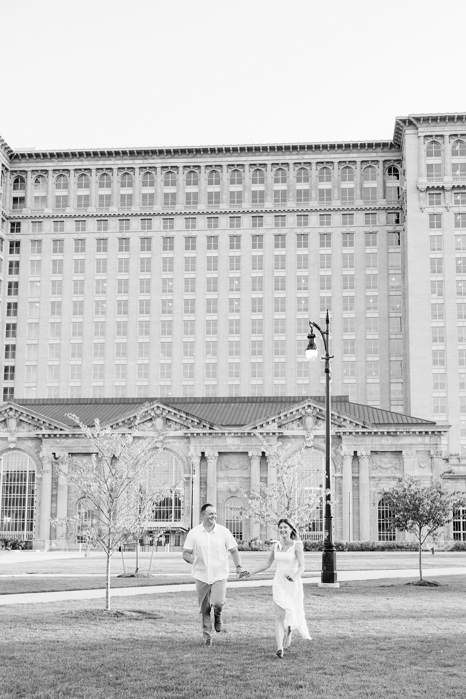 Engaged couple running and holding hands at Michigan Central Station summer engagement session in Detroit, MI