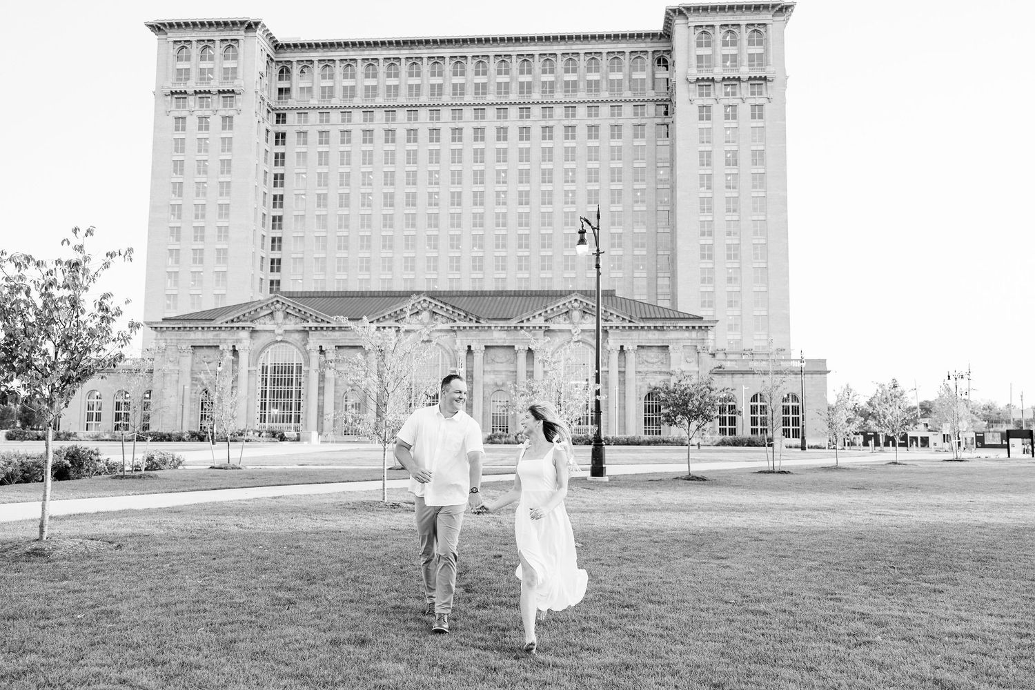 Engaged couple running and holding hands at Michigan Central Station summer engagement session in Detroit, MI