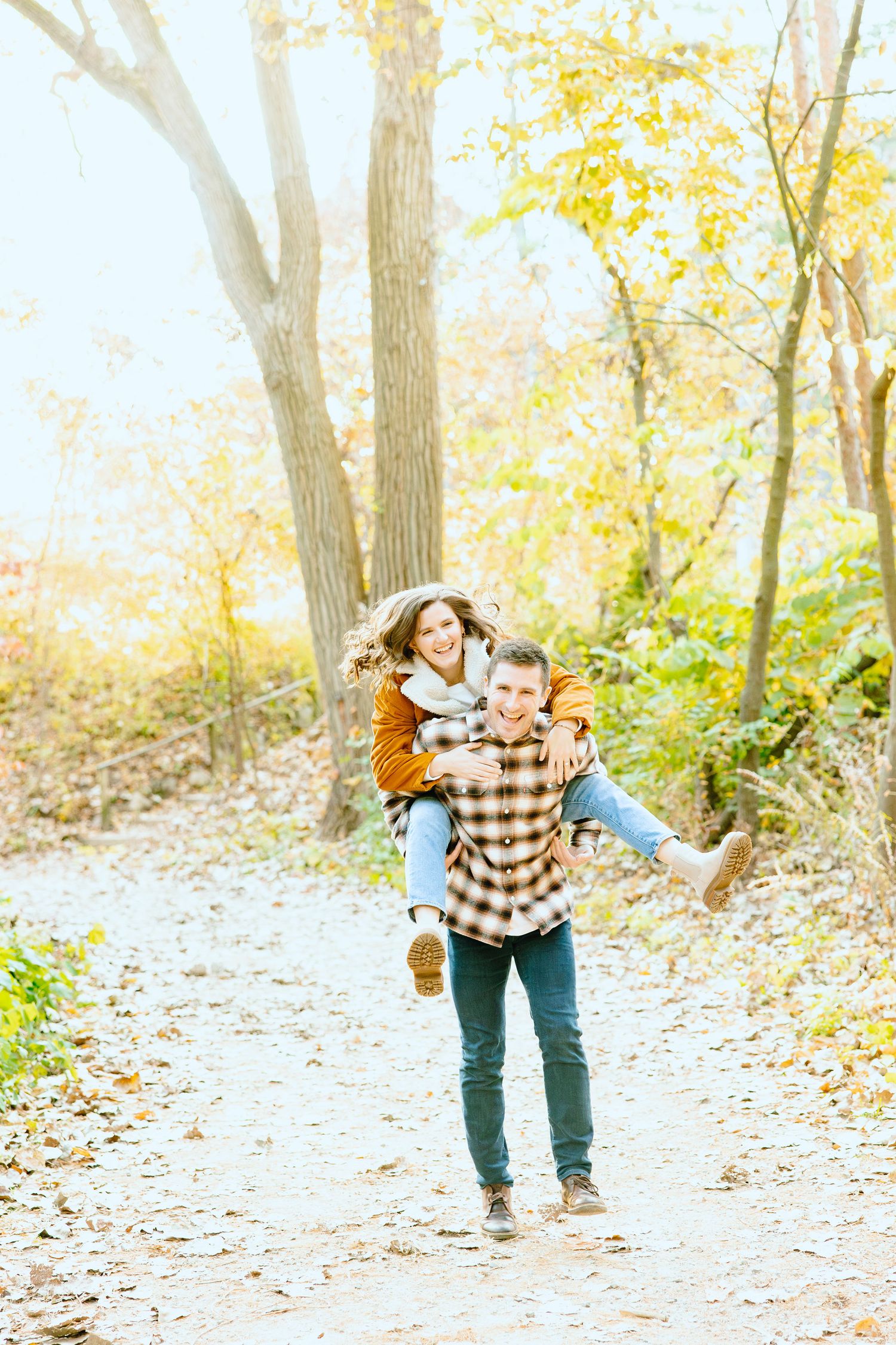 Man giving woman piggyback ride in forest at Nichols Arboretum fall engagement session in Ann Arbor, MI