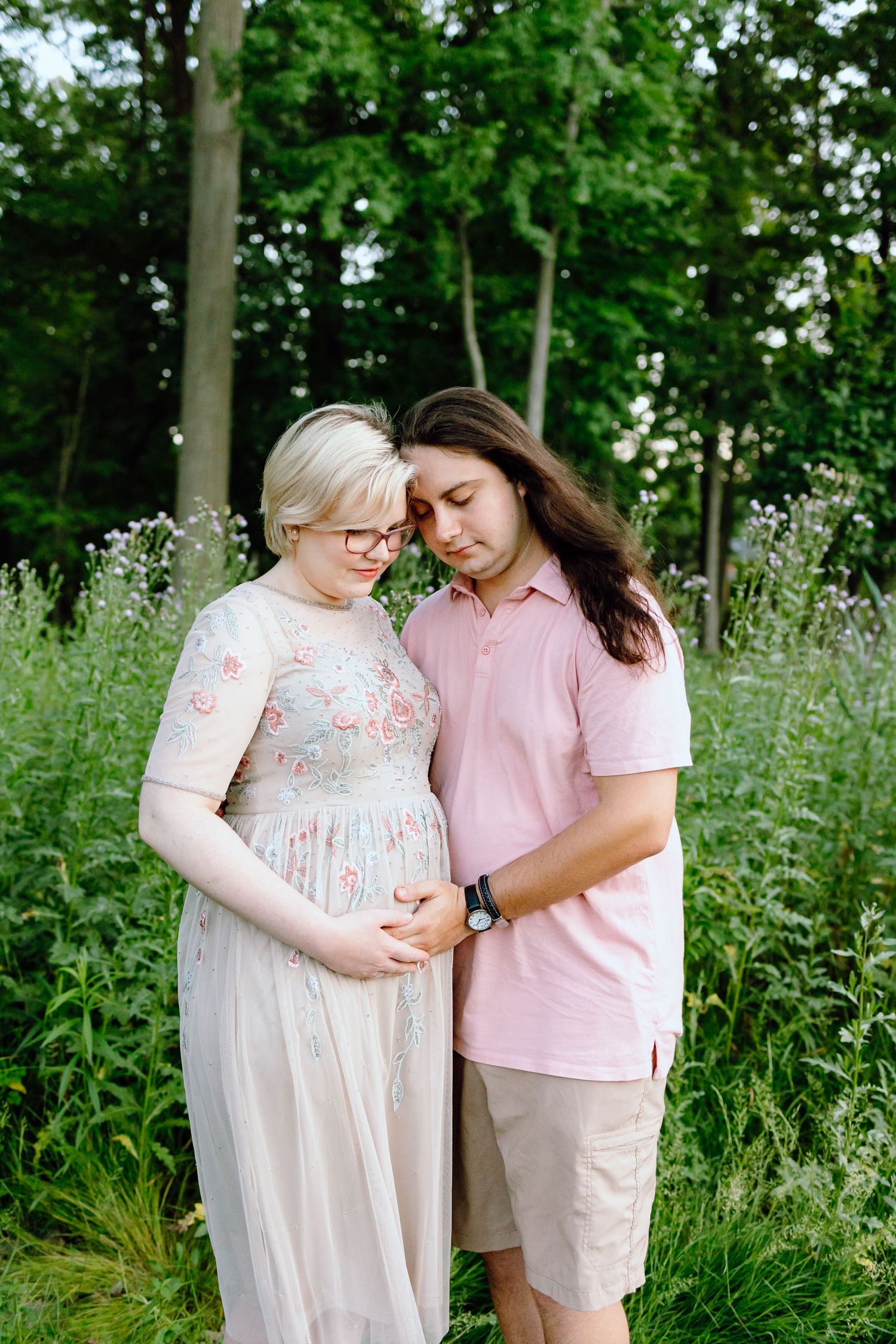 Pregnant couple embracing in front of thistle bush in Beverly Hills Village Park, MI
