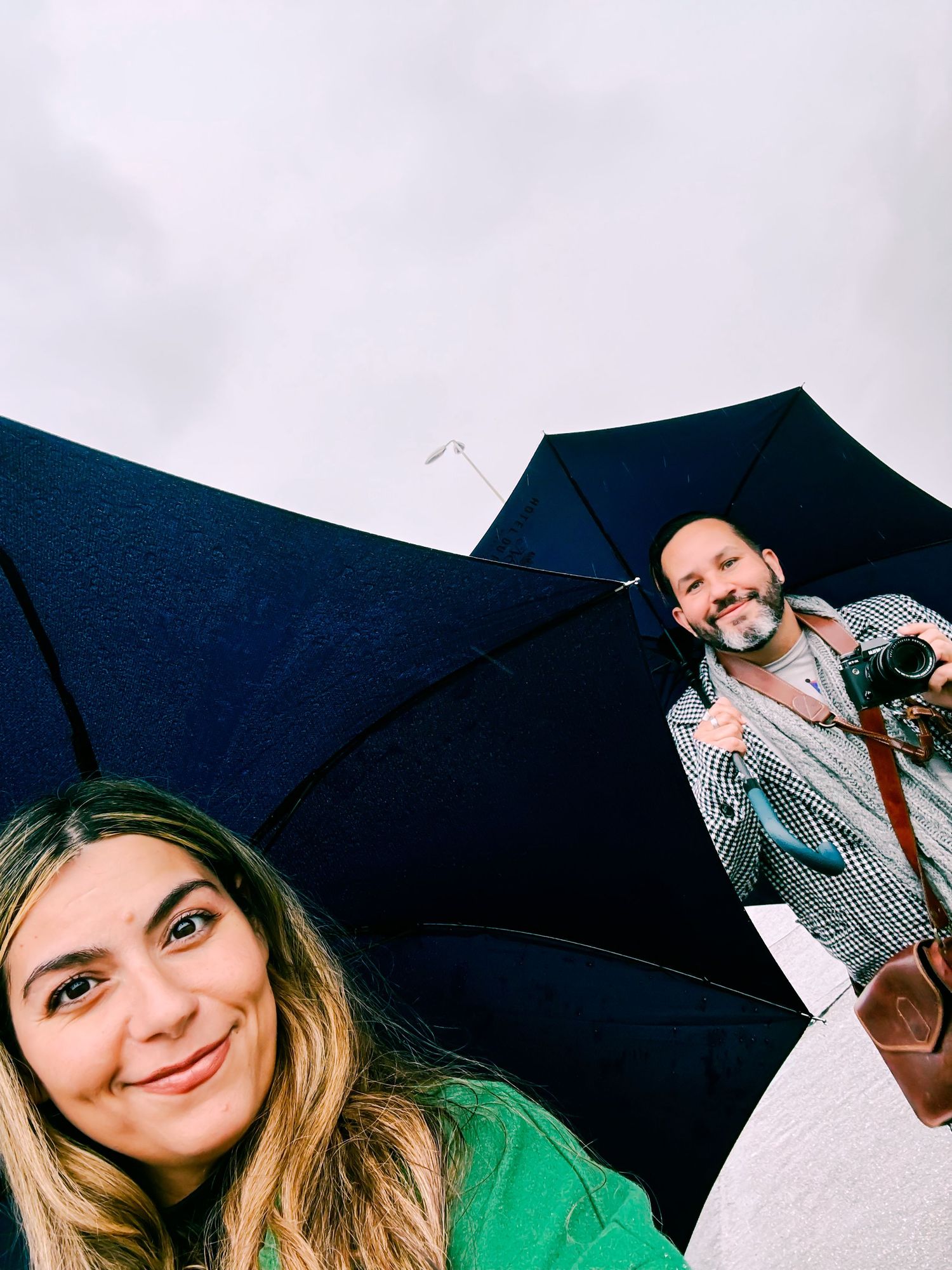 Two people posing with black umbrellas against an overcast sky.