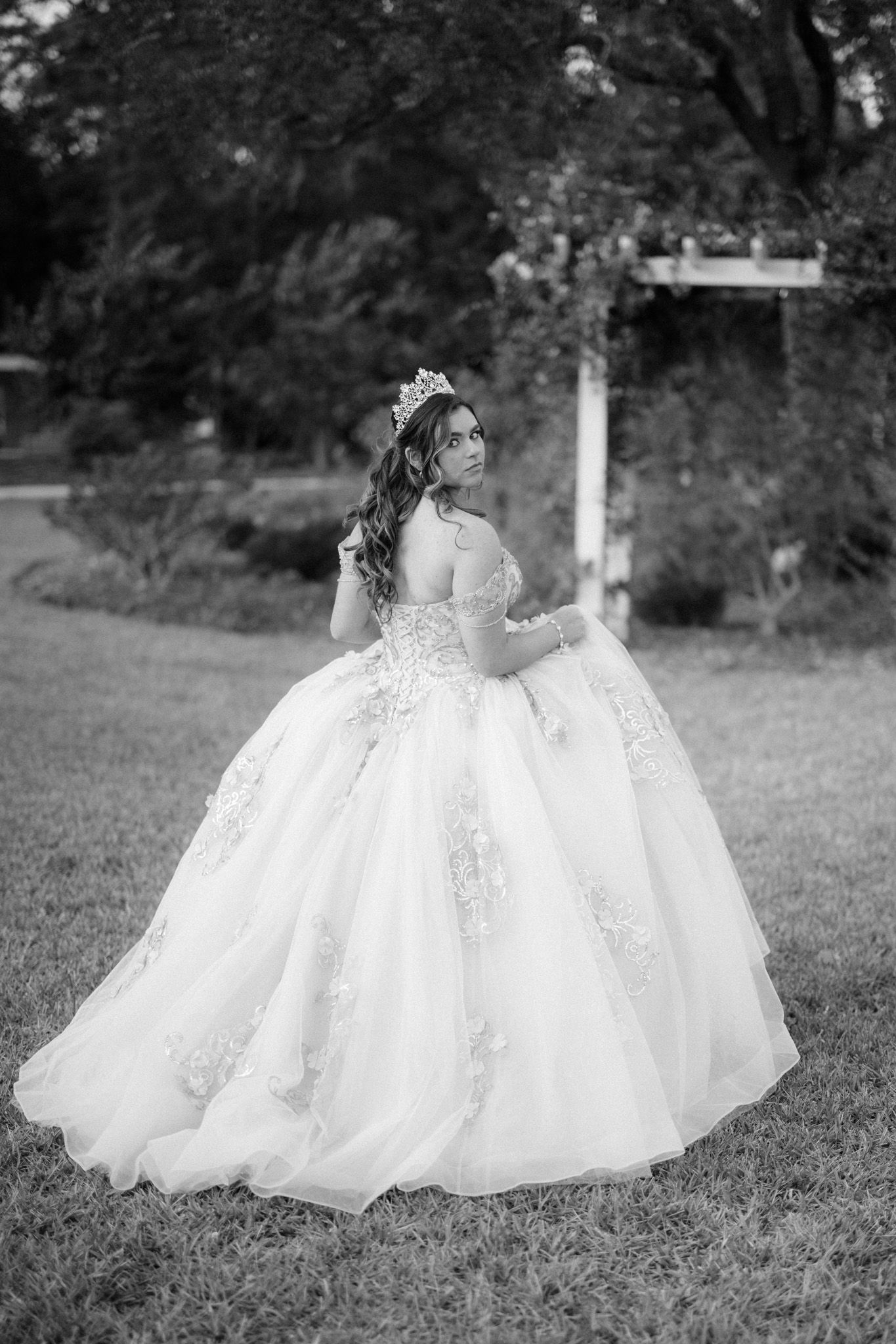 A dramatic black and white portrait of a ballgown wedding dress in a garden setting.