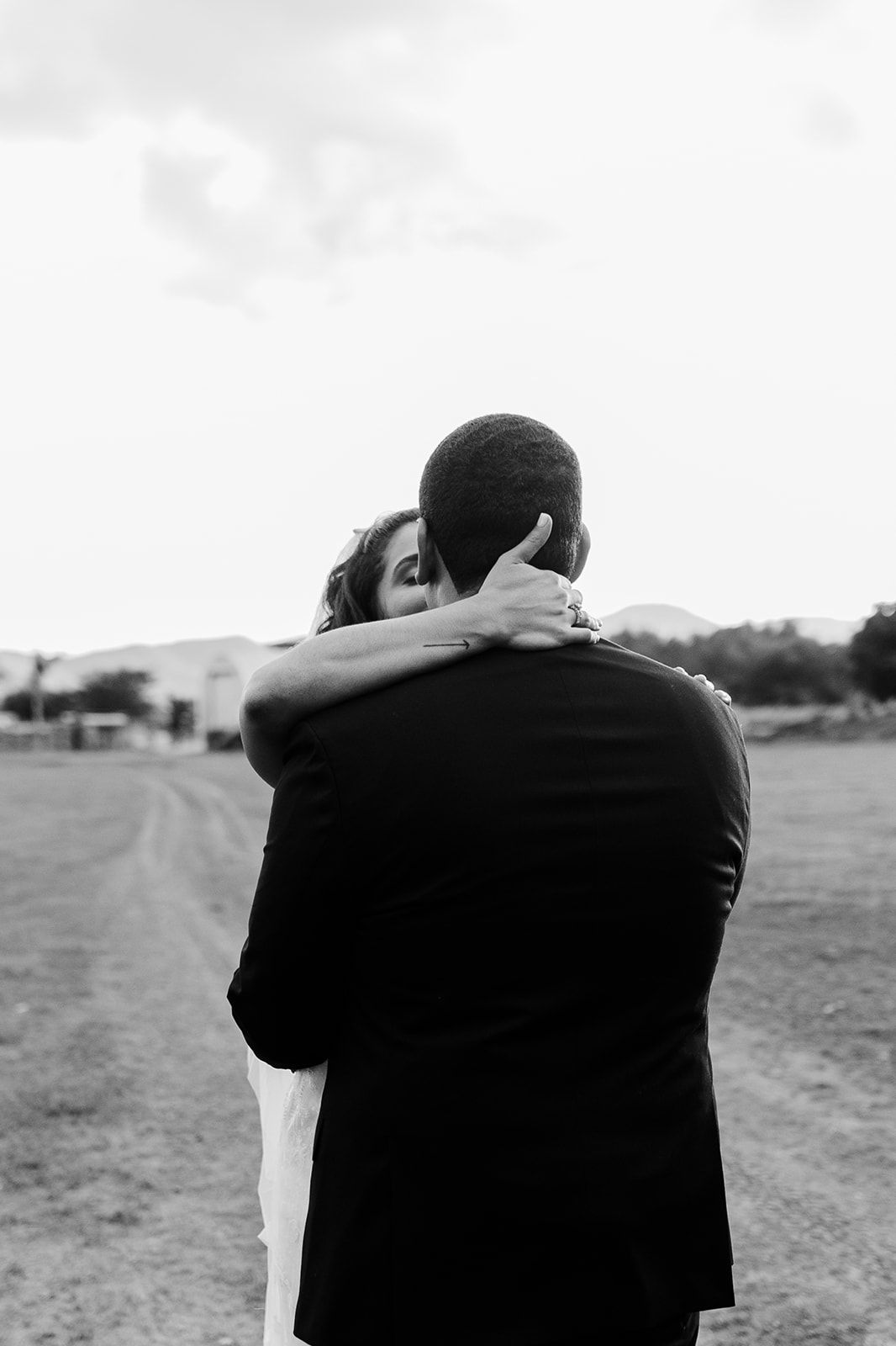 An intimate black and white wedding photo showing a tender embrace outdoors.