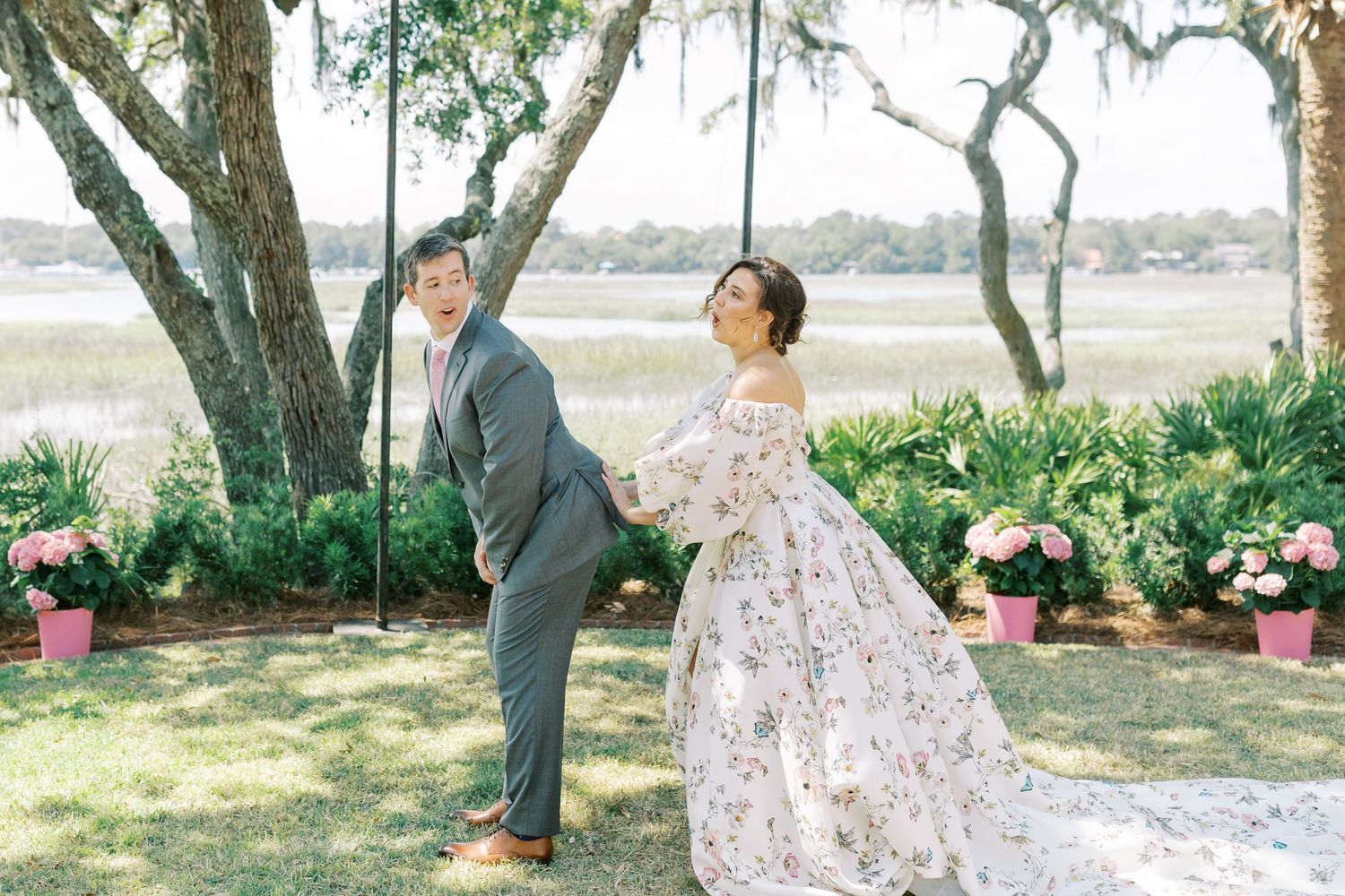 A romantic couple shares an intimate dance on the waterfront surrounded by pink flowers and lush greenery during an outdoor event.