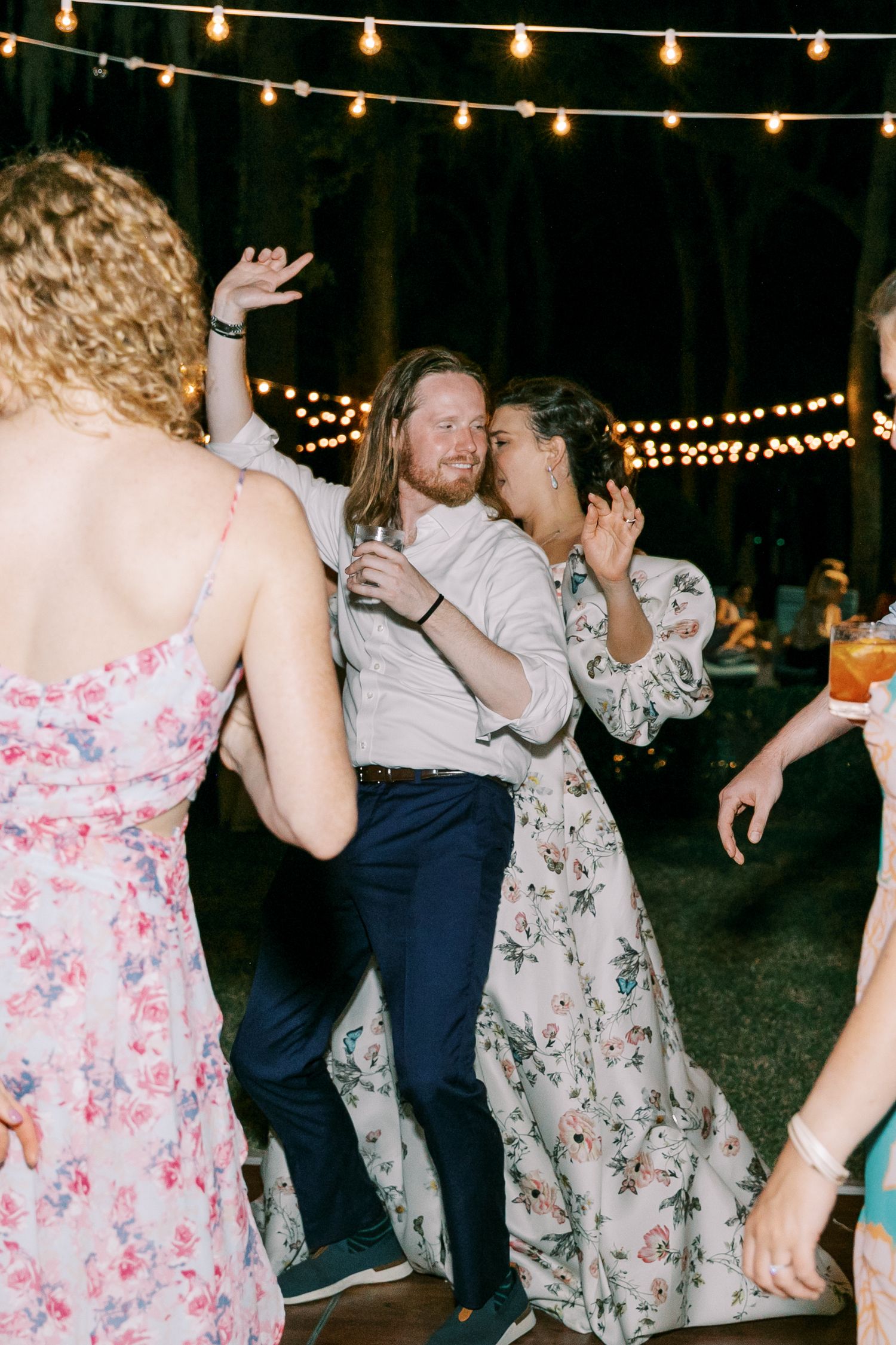 Guests dance under twinkling string lights at an outdoor evening wedding reception.