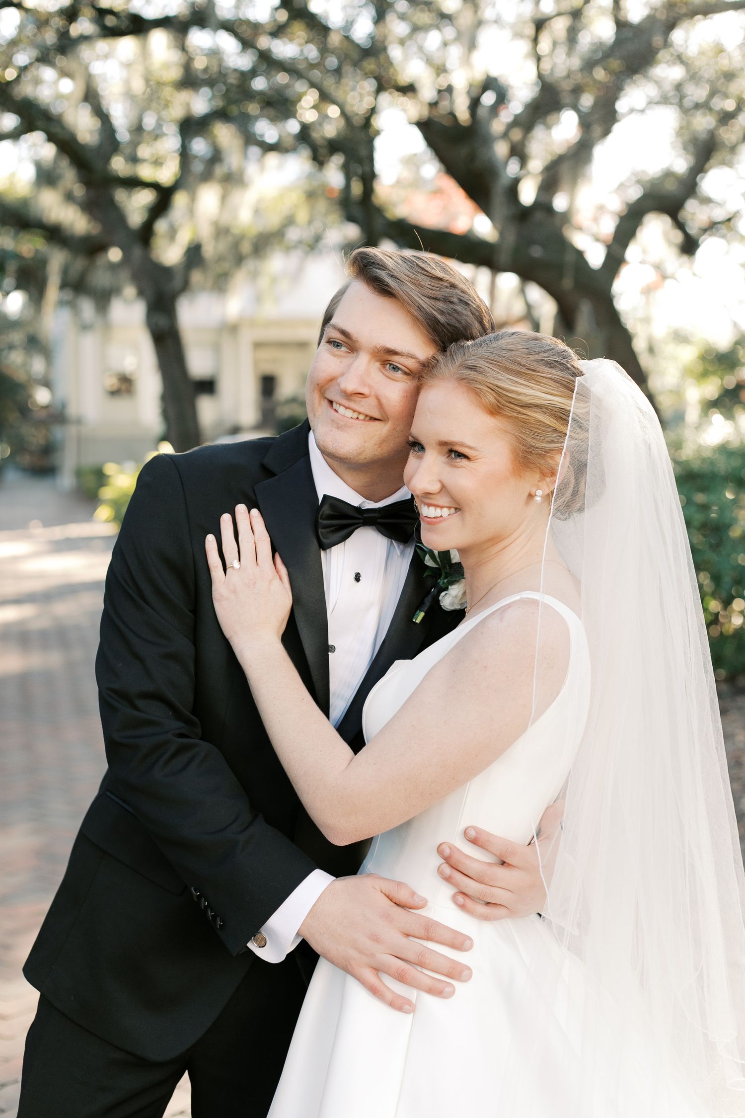 Elegant wedding couple sharing joyful moments outdoors under oak trees.