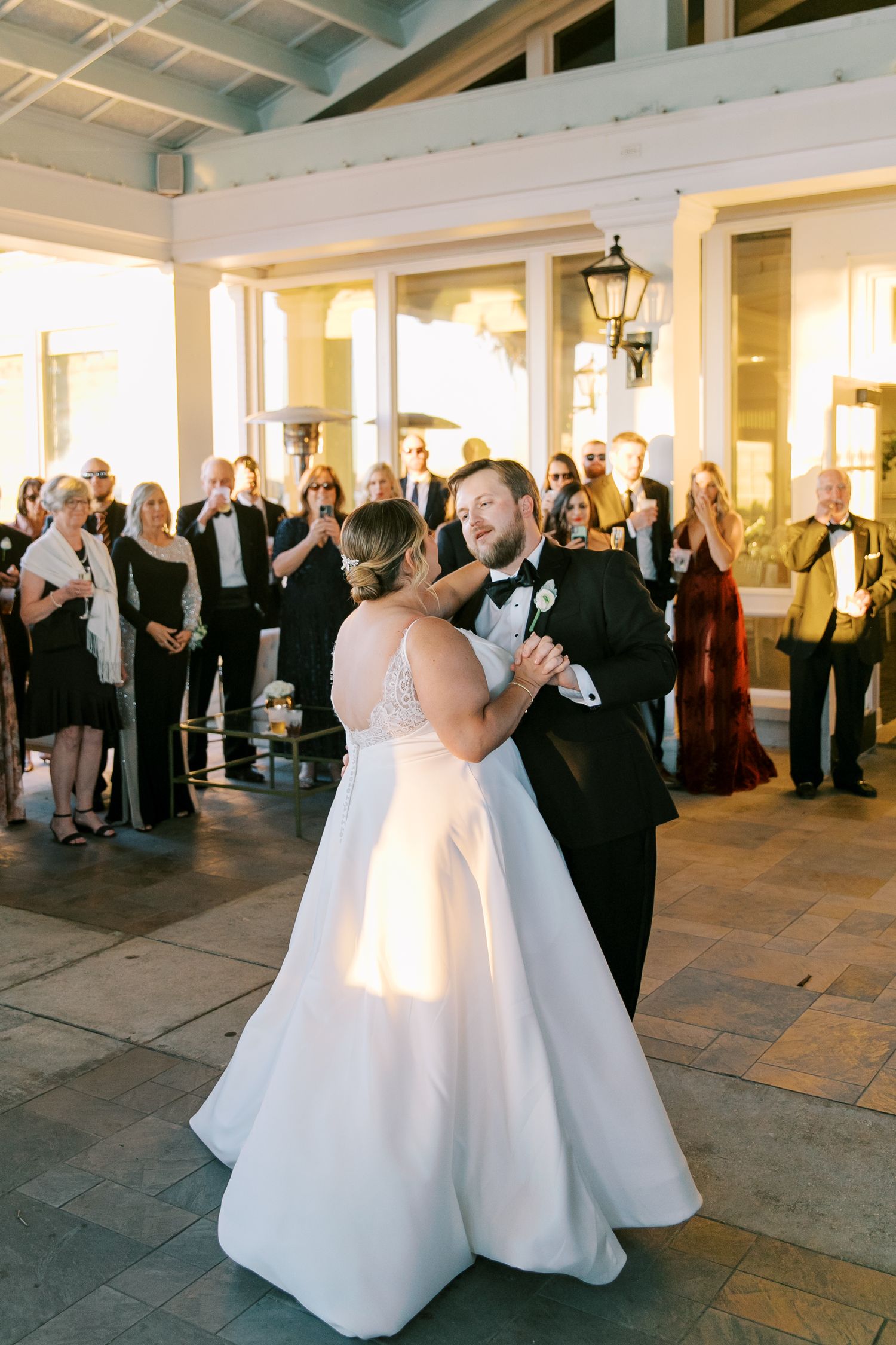 A couple shares their first dance at an evening wedding reception on an outdoor covered patio.