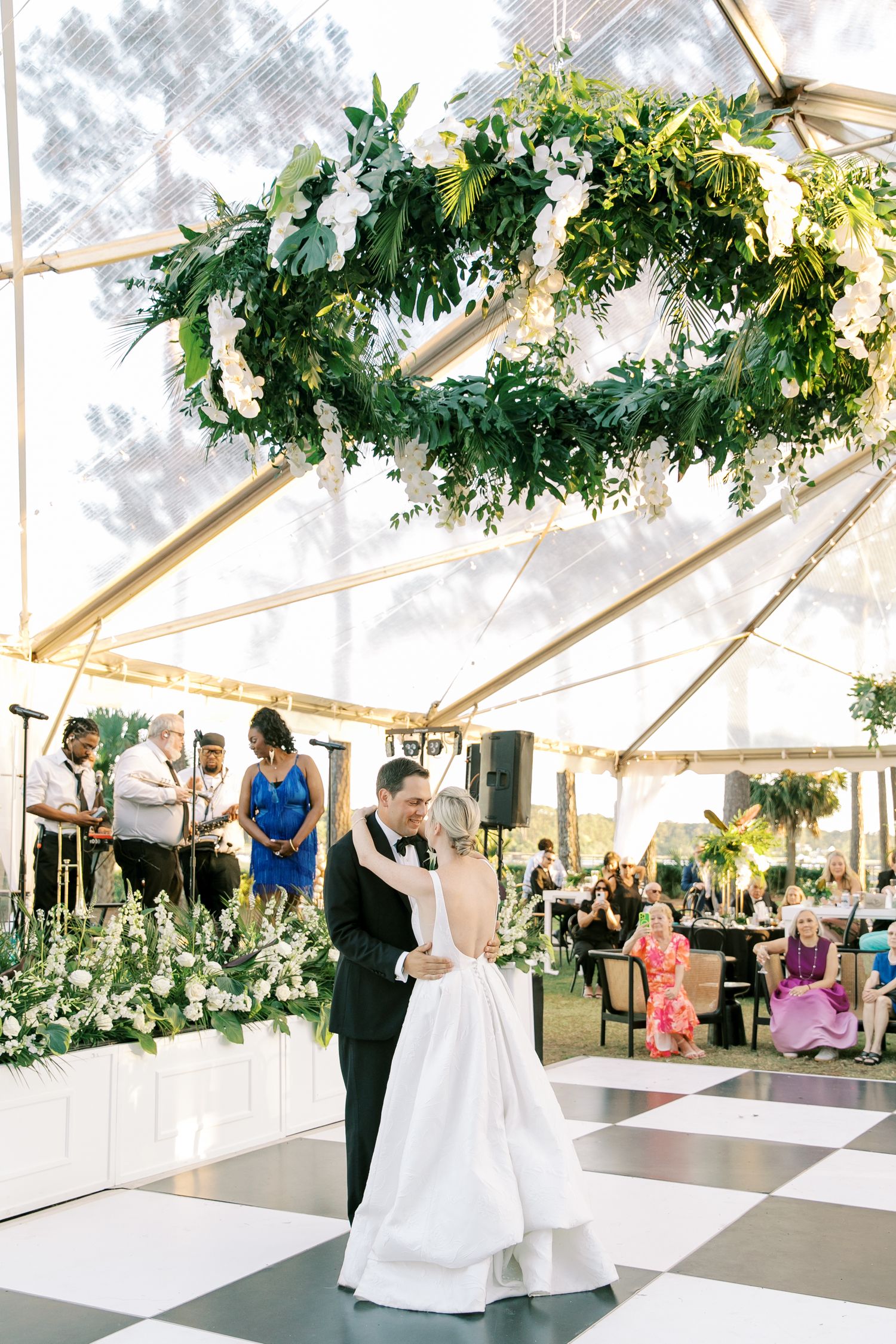 First dance under a clear tent with lush greenery chandelier and checkered dance floor at the Oldfield Golf Club in Bluffton.