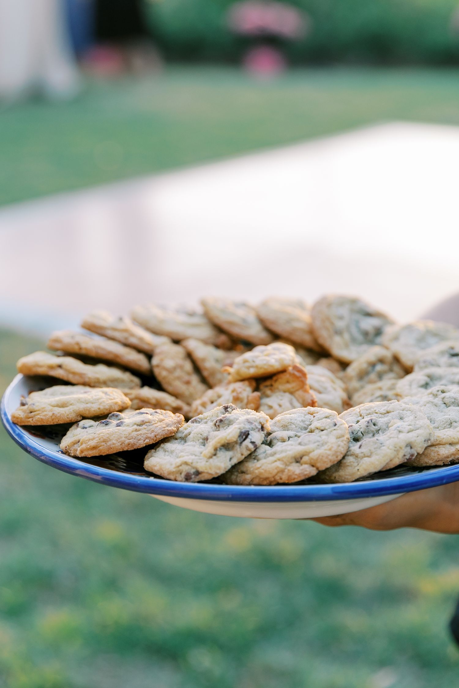 A blue plate filled with freshly baked chocolate chip cookies being held outdoors.