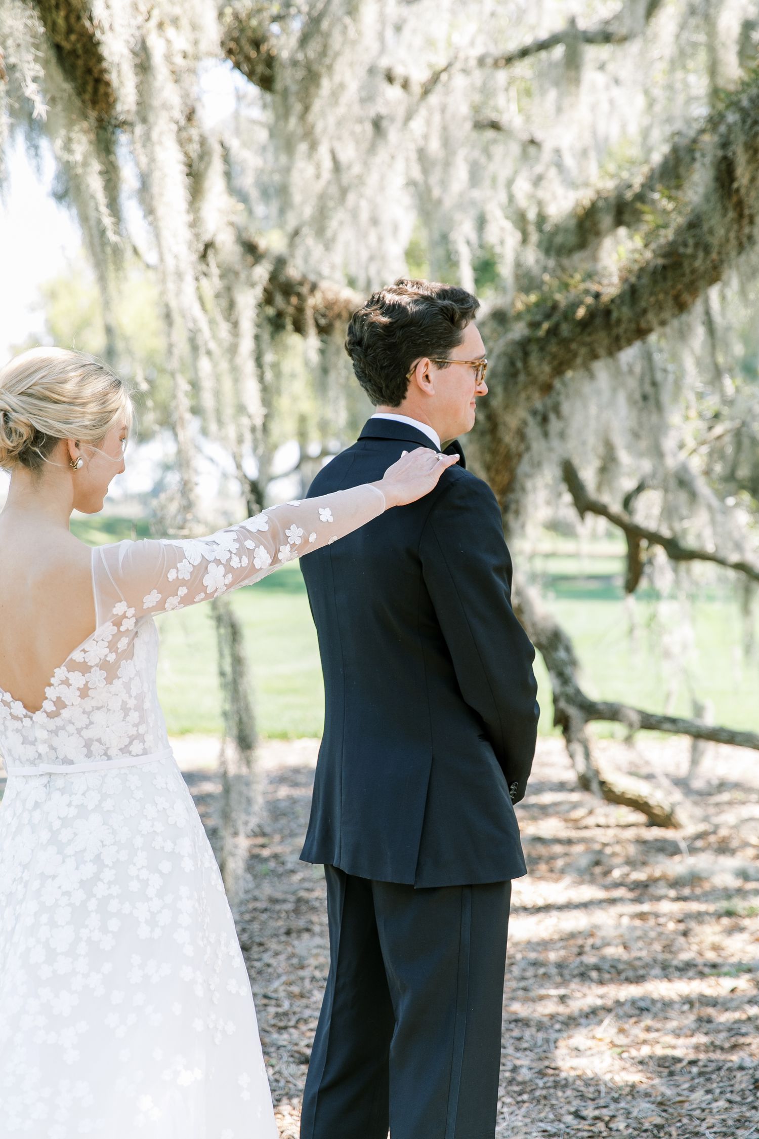 A couple shares a romantic first look moment under Spanish moss draped trees at an outdoor wedding venue.