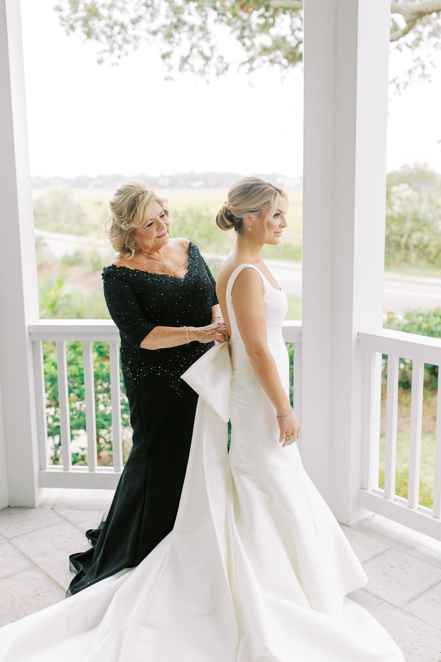 A wedding dress fitting moment on an elegant white porch with a flowing gown and formal black evening dress.