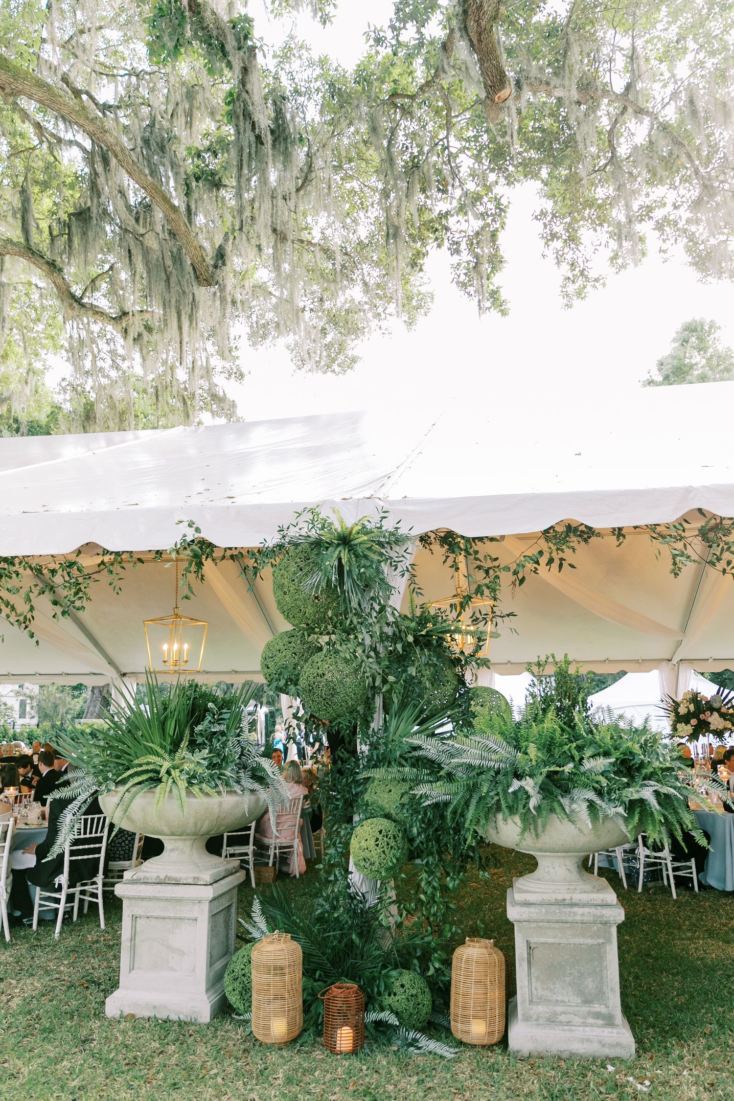 Elegant outdoor wedding reception setup under Spanish moss with white tent and lush greenery decorations.
