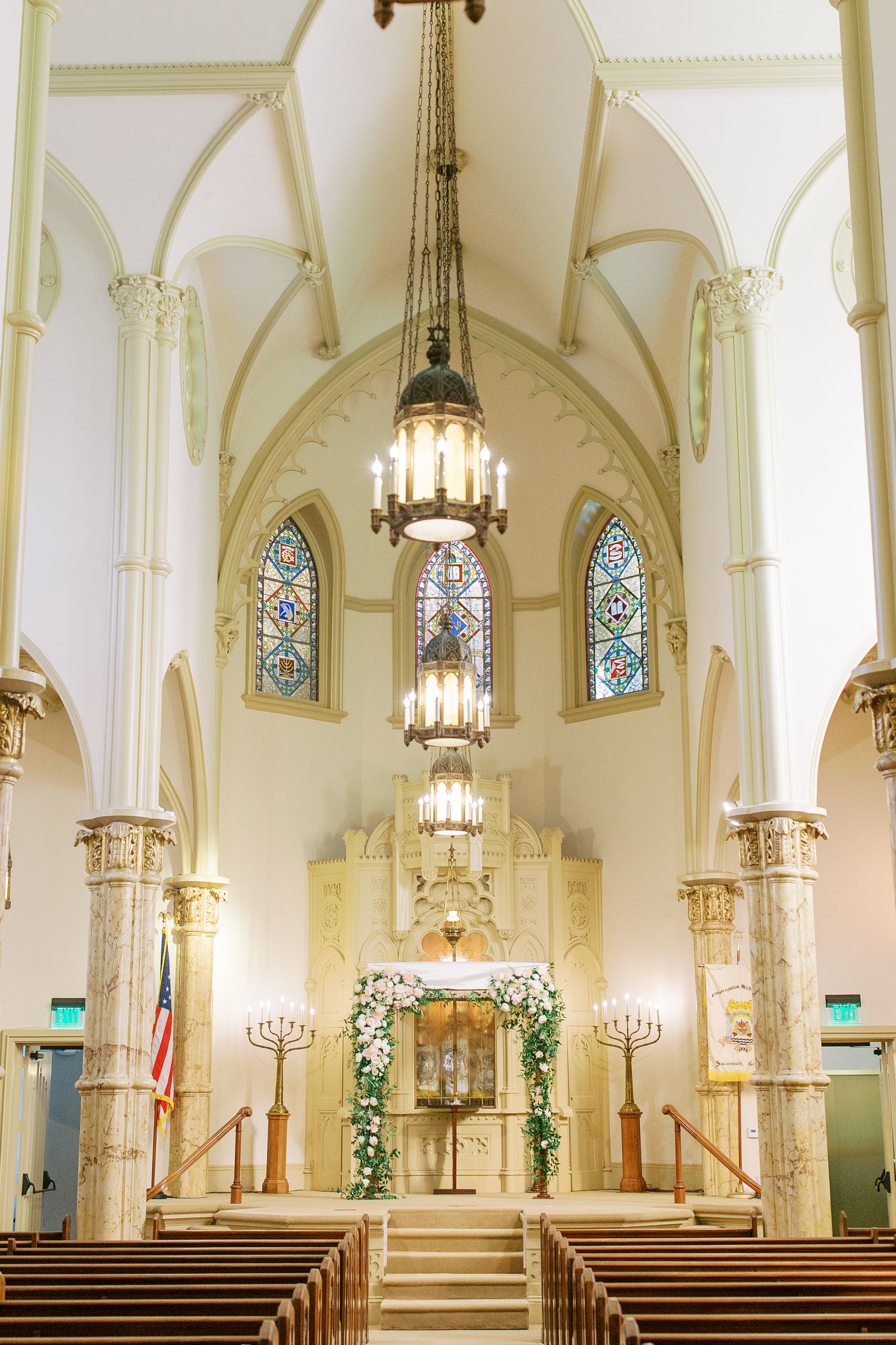 Interior of a Gothic church with vaulted ceilings, stained glass windows and decorative floral arch.