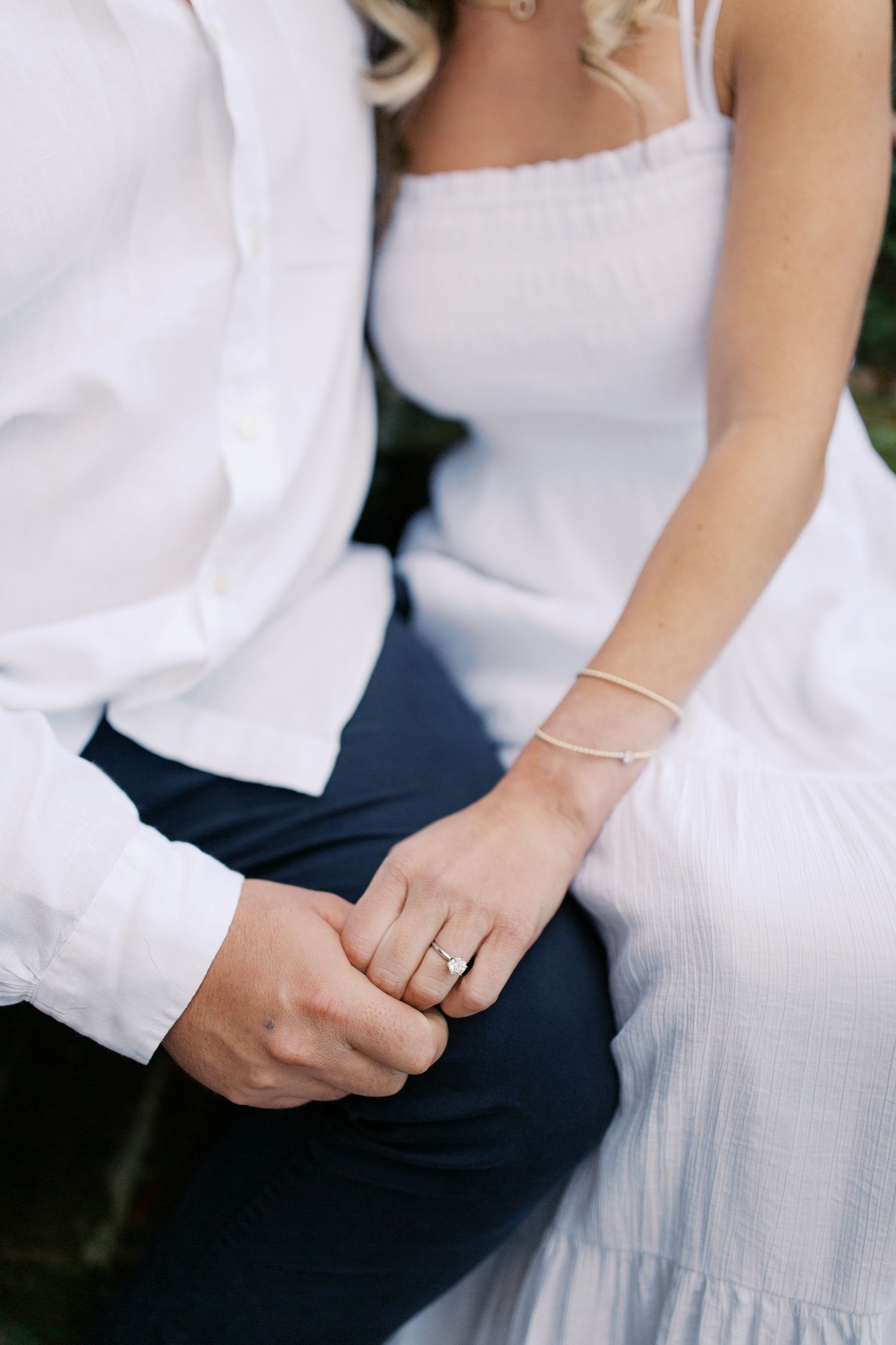 Close-up of hands showing an engagement ring with white dress and formal attire details.