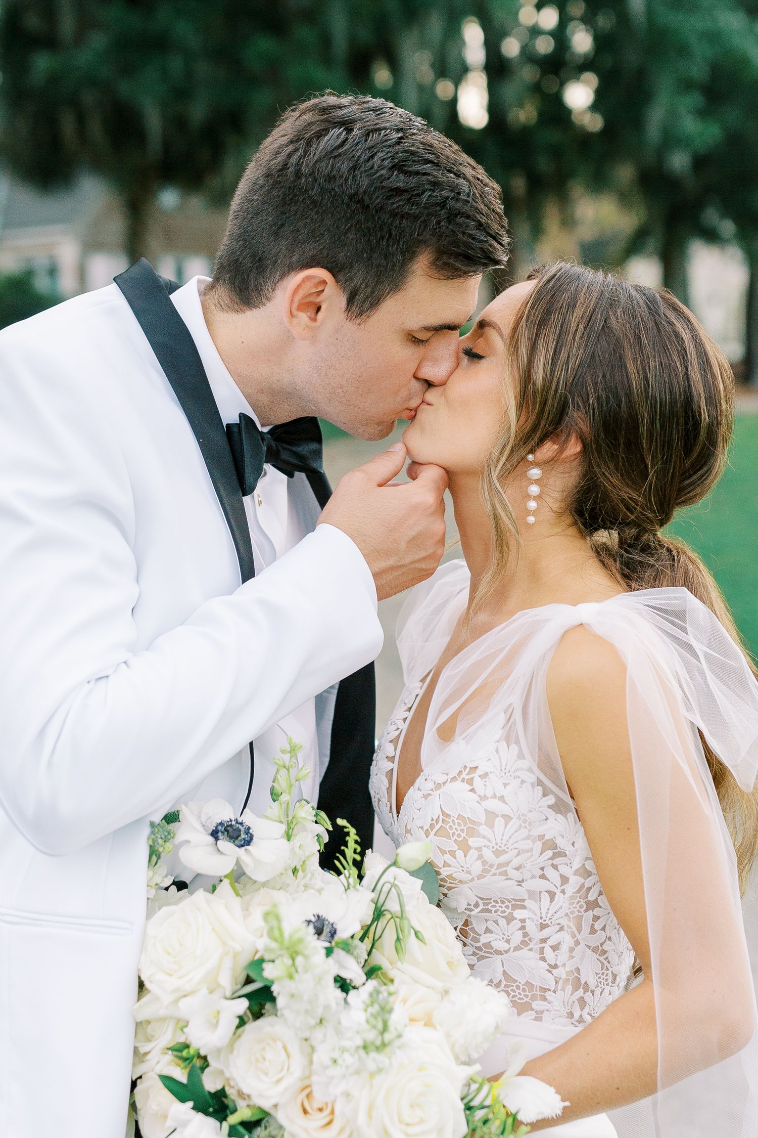Romantic wedding couple sharing a kiss while holding a white rose bouquet.