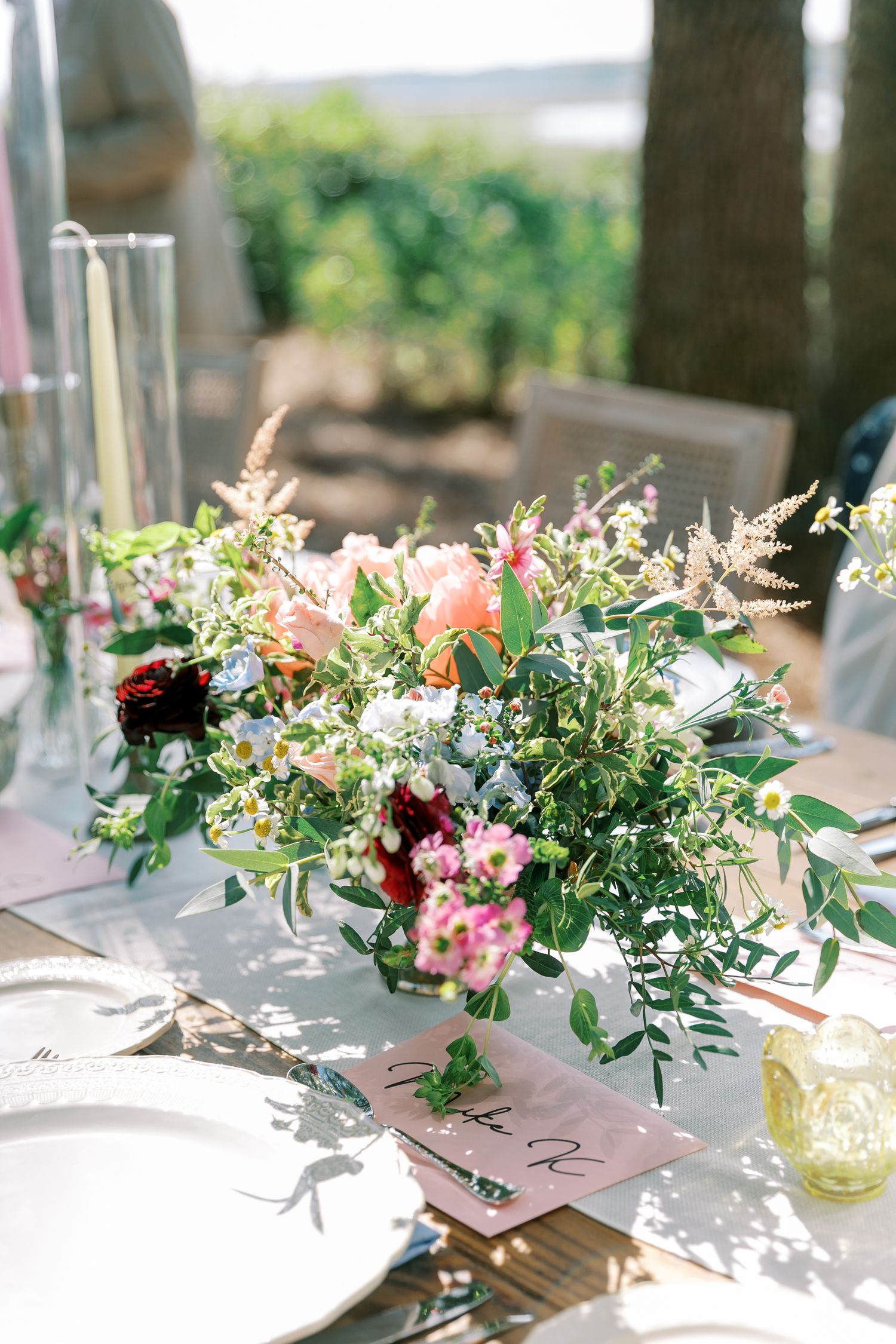 Elegant floral centerpiece with pink and burgundy blooms on an outdoor wedding reception table.