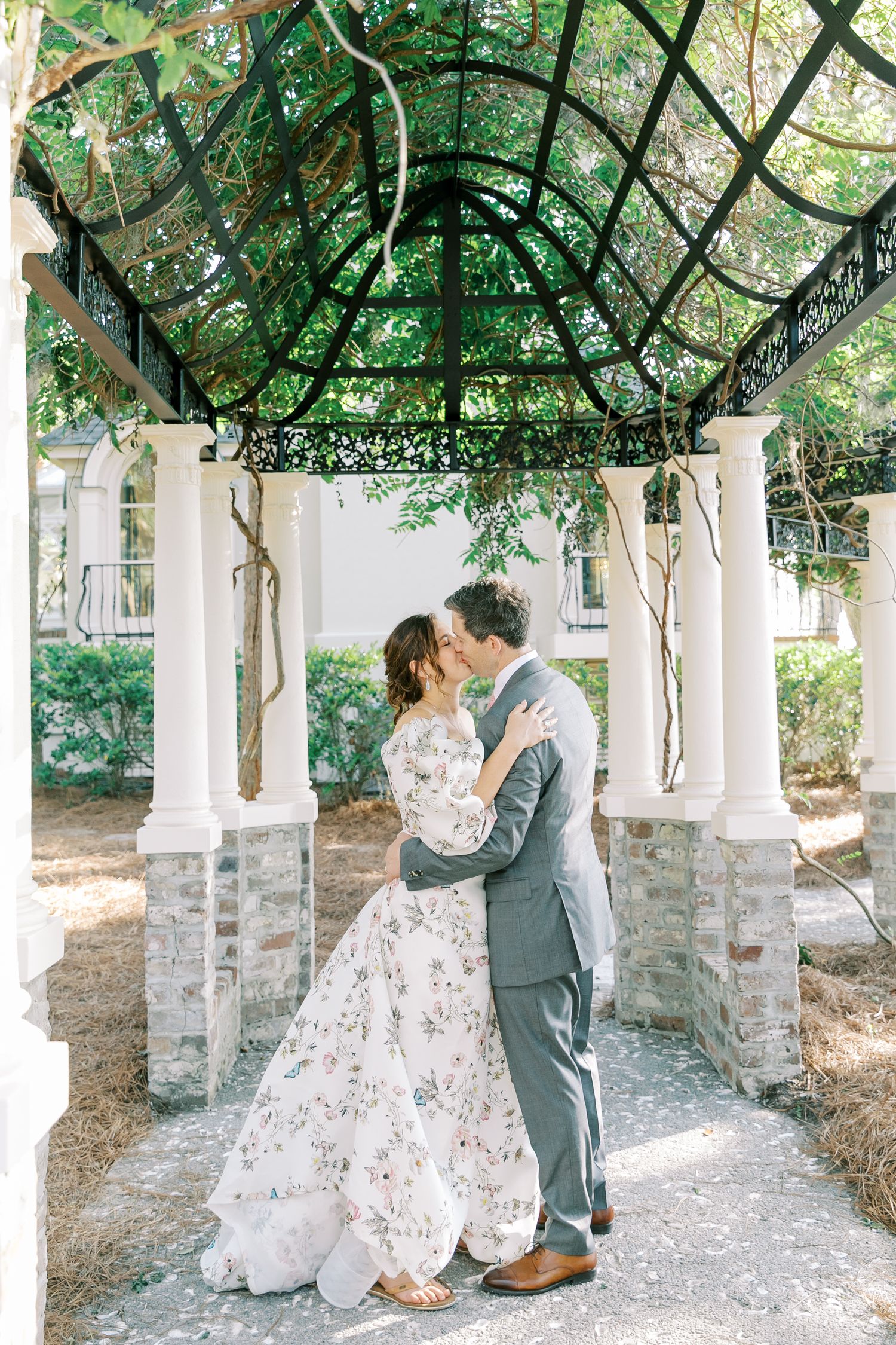 A romantic moment captured under a vine-covered pergola at an elegant outdoor wedding.