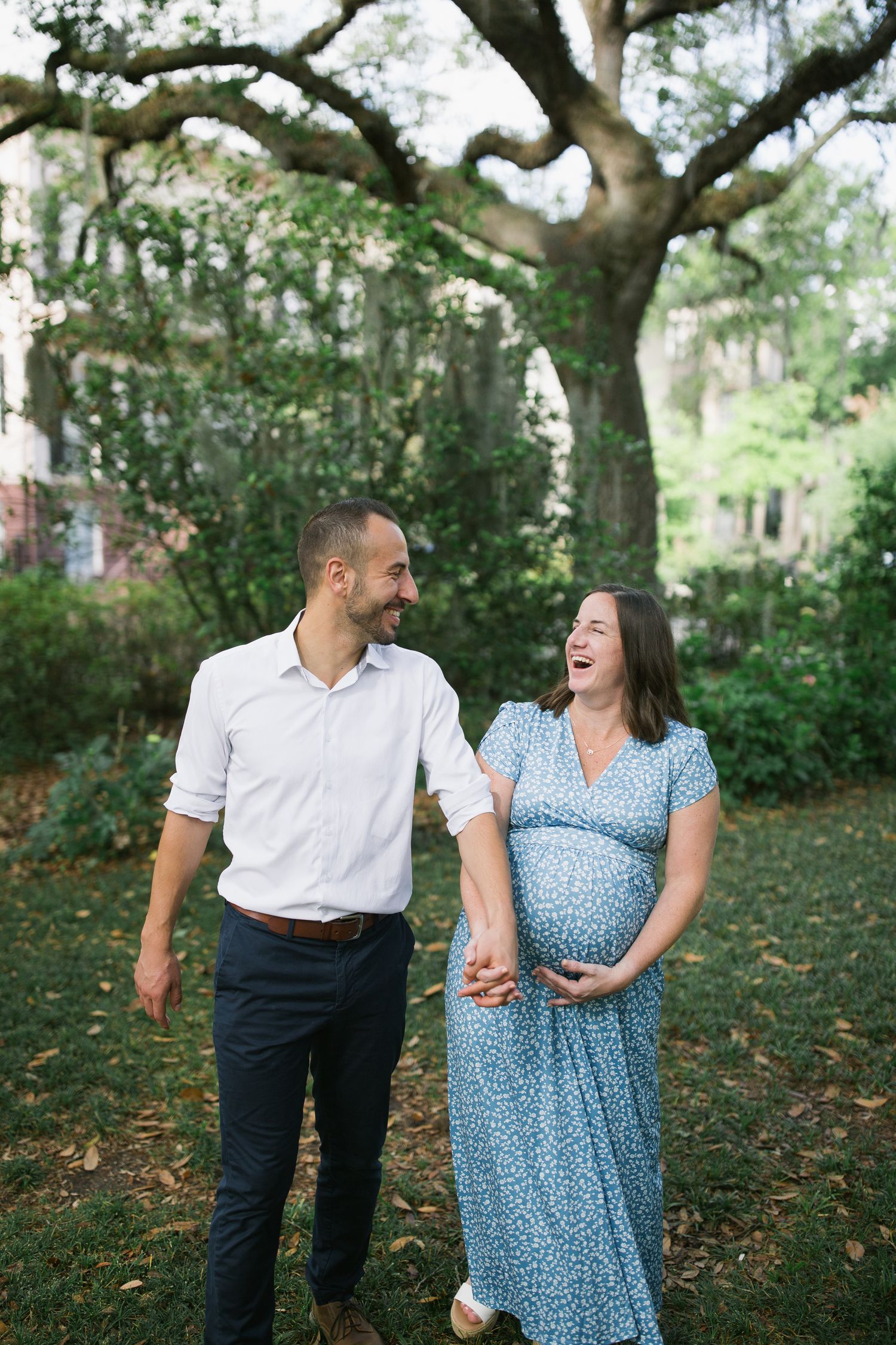 Couple sharing intimate moments under large oak trees in outdoor maternity photoshoot.