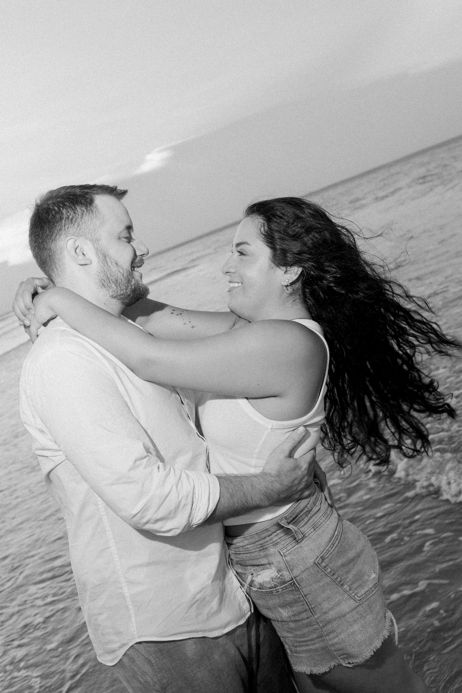 Couple dancing and twirling in the ocean waves, captured in a series of joyful black and white photos.