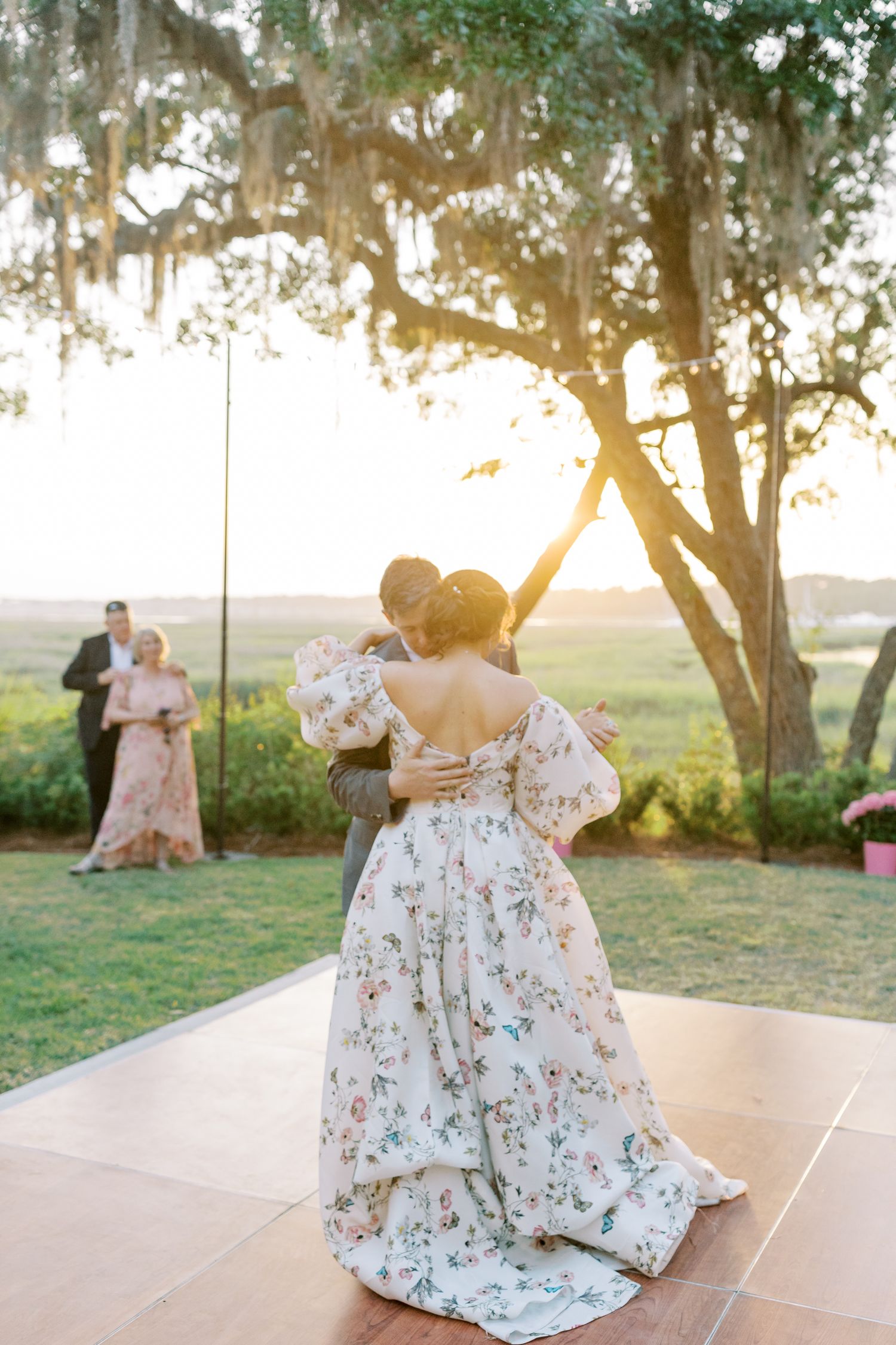 Couples dancing on an outdoor dance floor at sunset under Spanish moss draped trees.