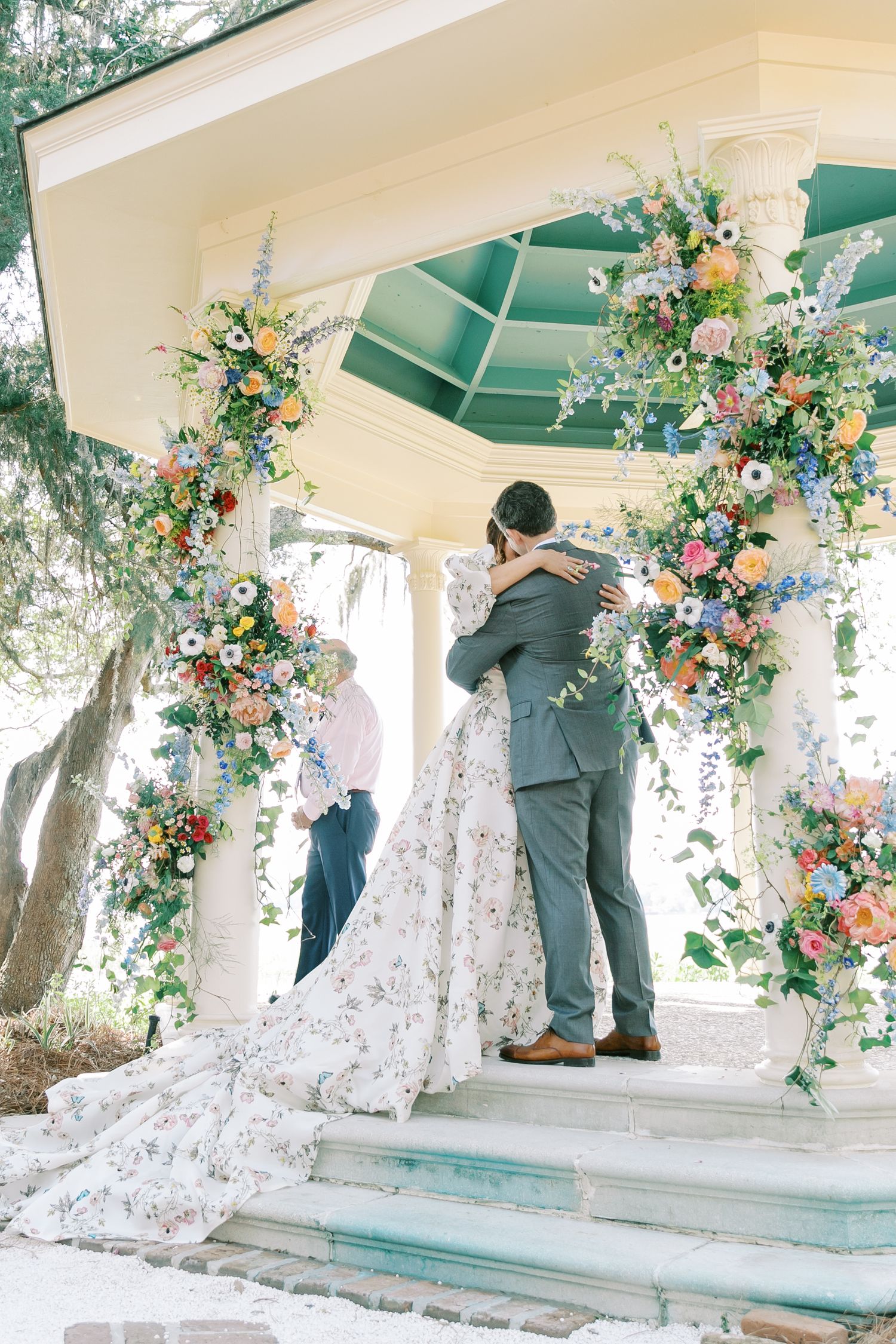 Wedding ceremony in a white gazebo decorated with colorful floral arrangements.